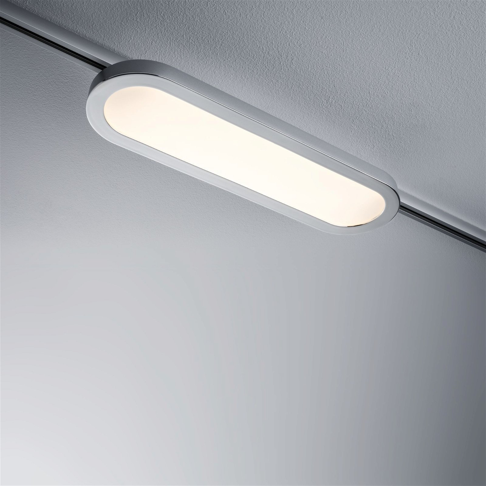 Un apparecchio di illuminazione ovale argentato è montato su una guida contro un soffitto grigio.
