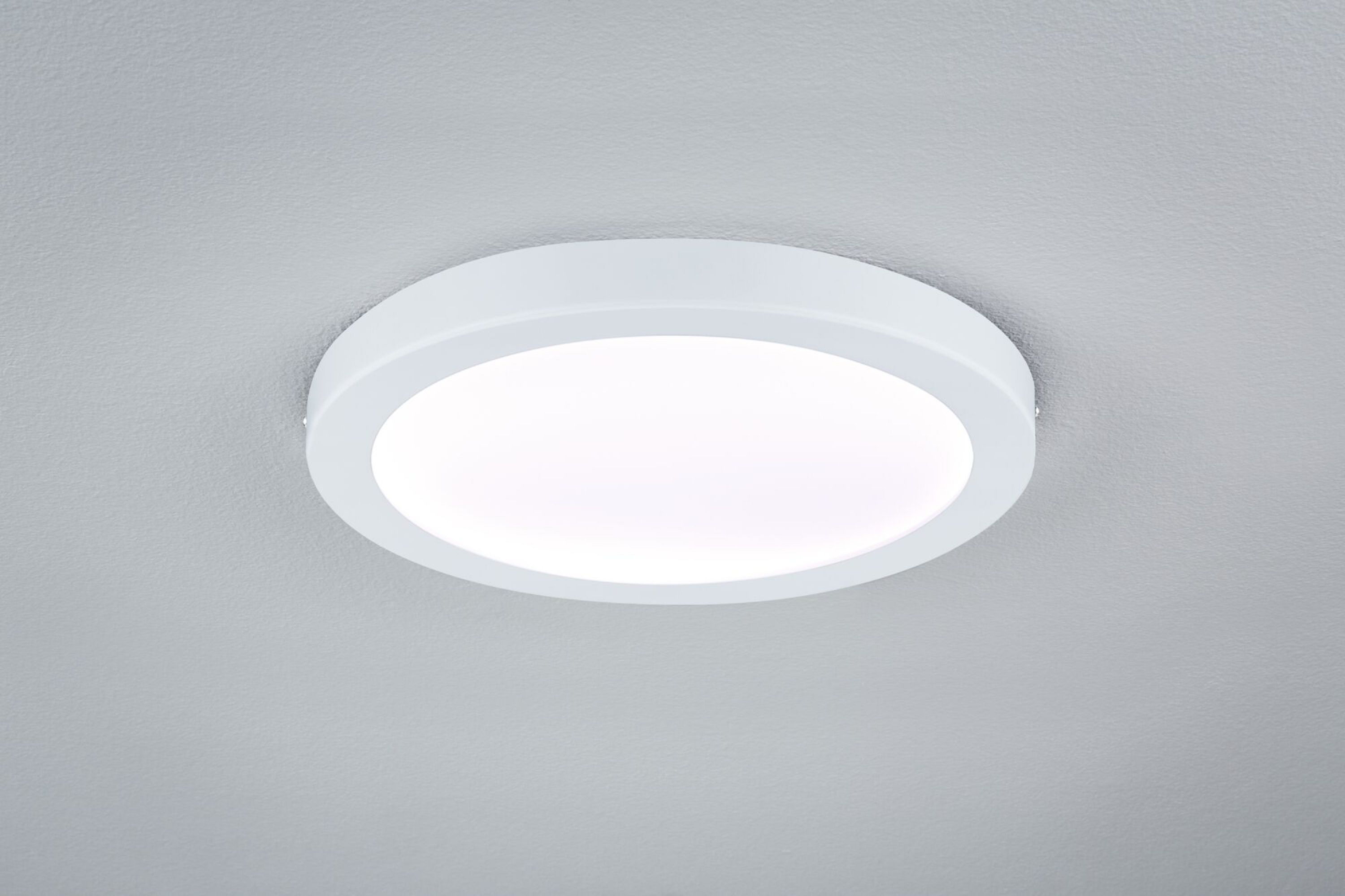 Un apparecchio di illuminazione a soffitto rotondo bianco, montato a filo su un soffitto grigio chiaro, che emette una luce soffusa.