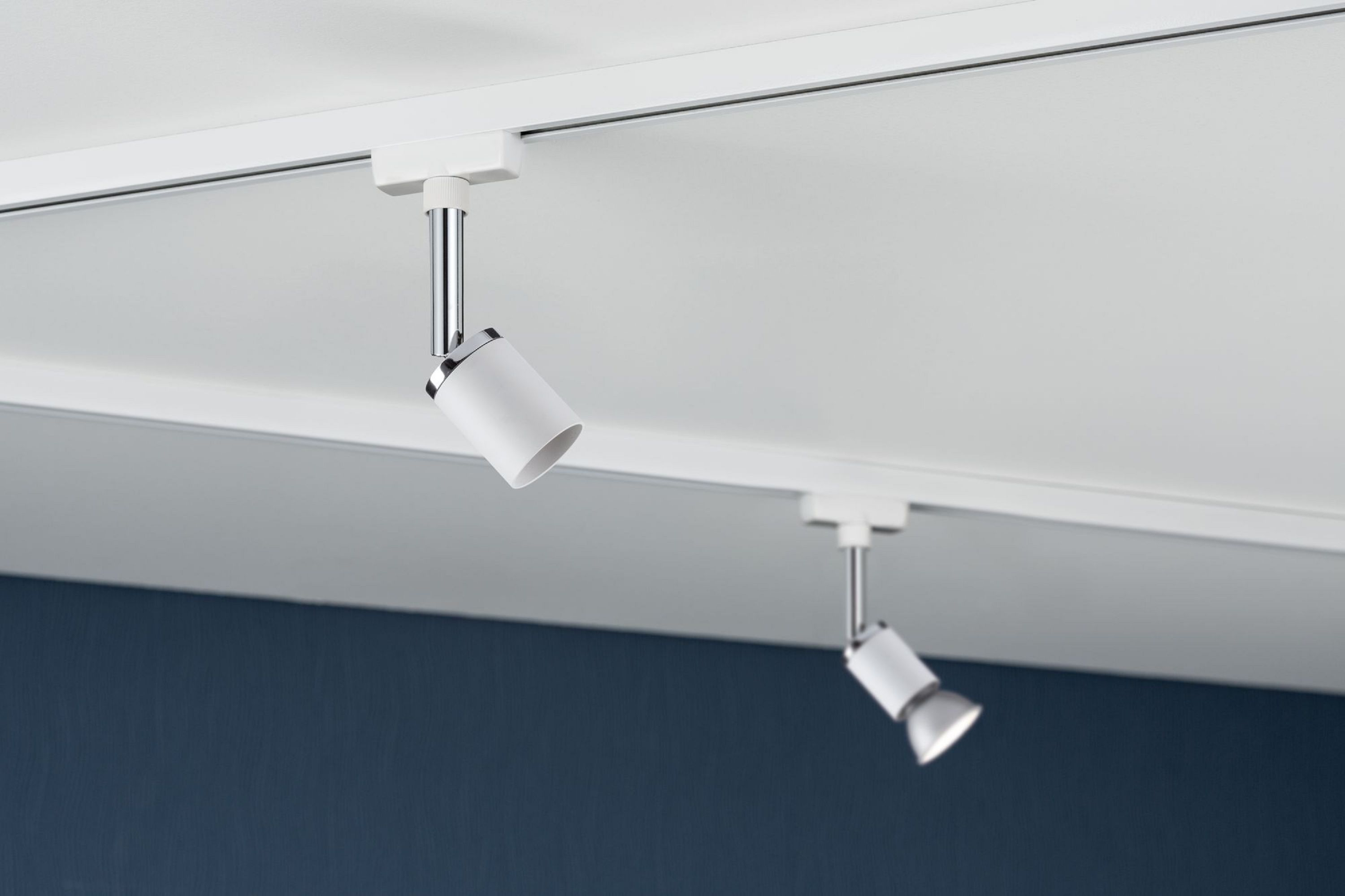 Due faretti bianchi su un soffitto bianco contro un muro blu navy.
