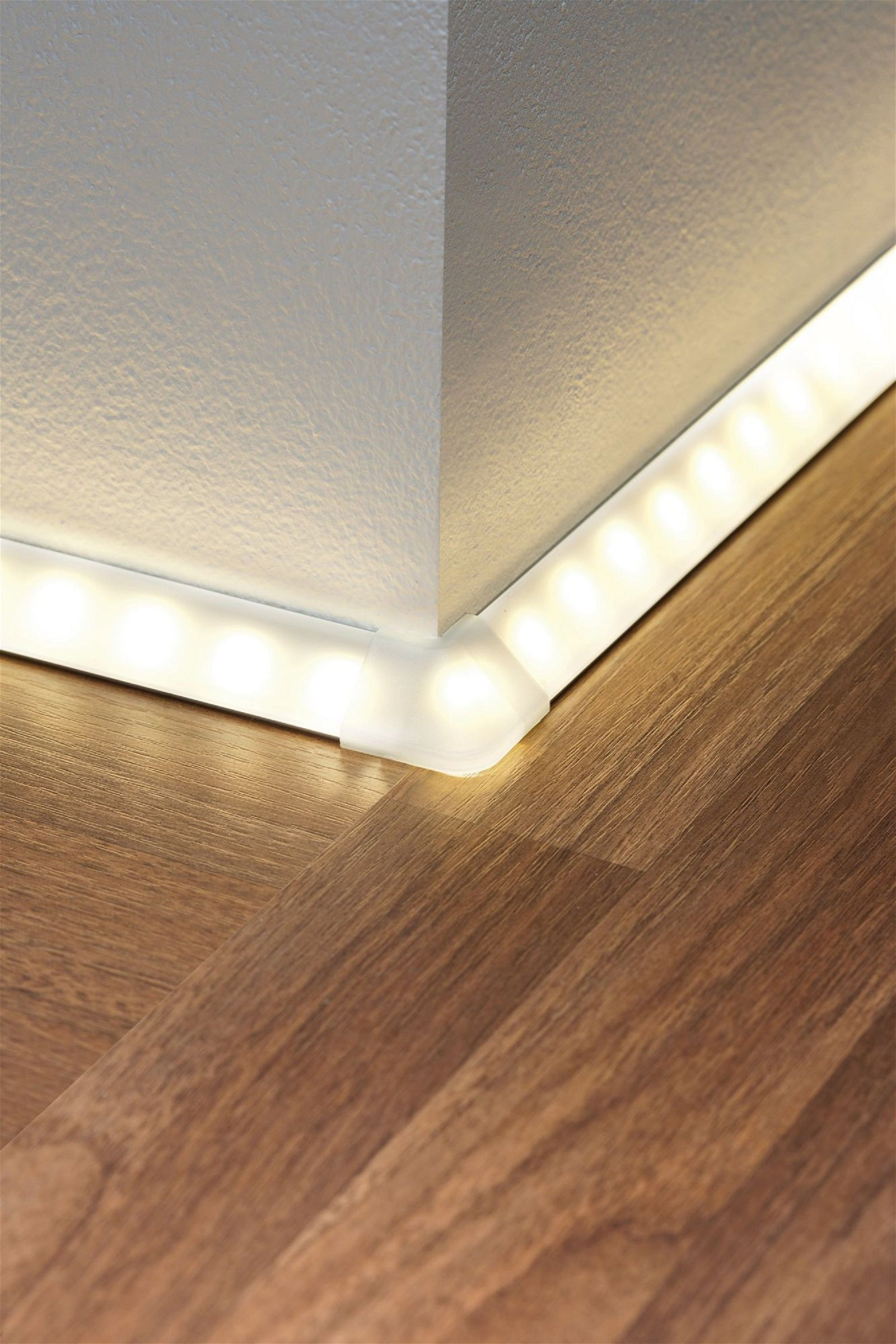 Éclairage à bandes LED installé le long du coin d'un mur blanc et d'un plancher en bois.