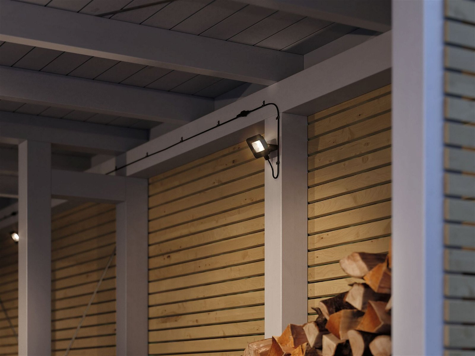 Szene im Freien: Leuchte an Holzwand. Holzstapel im Hintergrund.