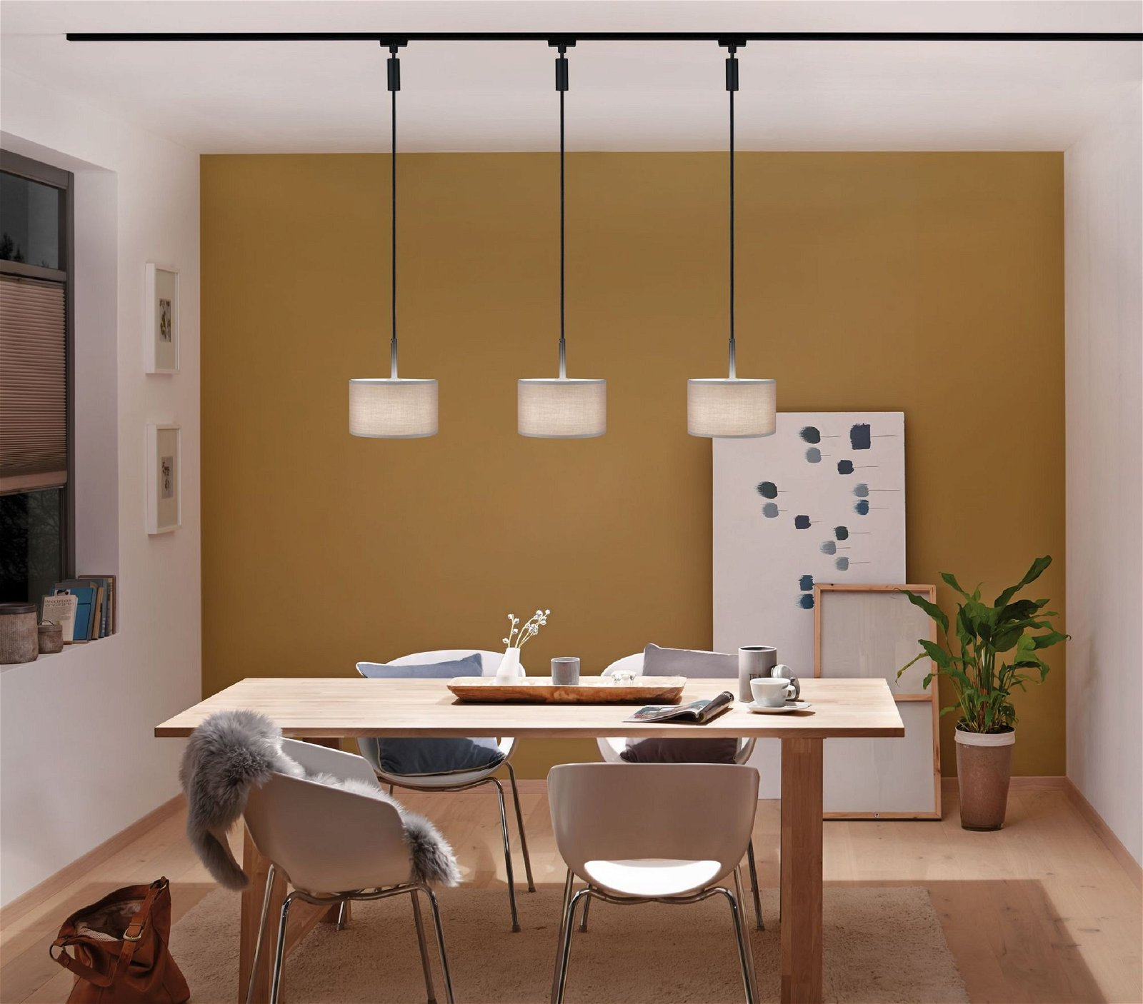 Ein Essbereich mit einem Holztisch, drei Pendelleuchten und einer senfgelben Wand.