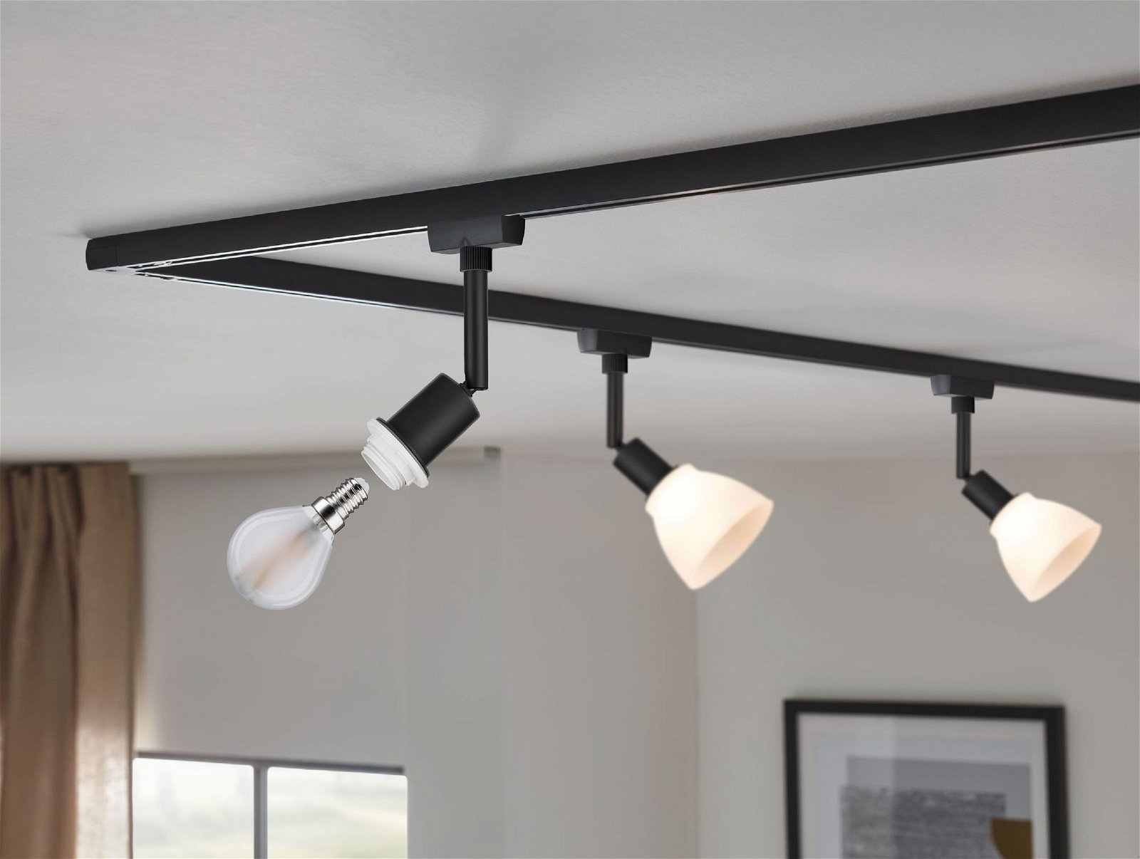 Schienenbeleuchtung mit drei Lampen, eine mit eingesetzter Glühbirne, an weißer Decke.