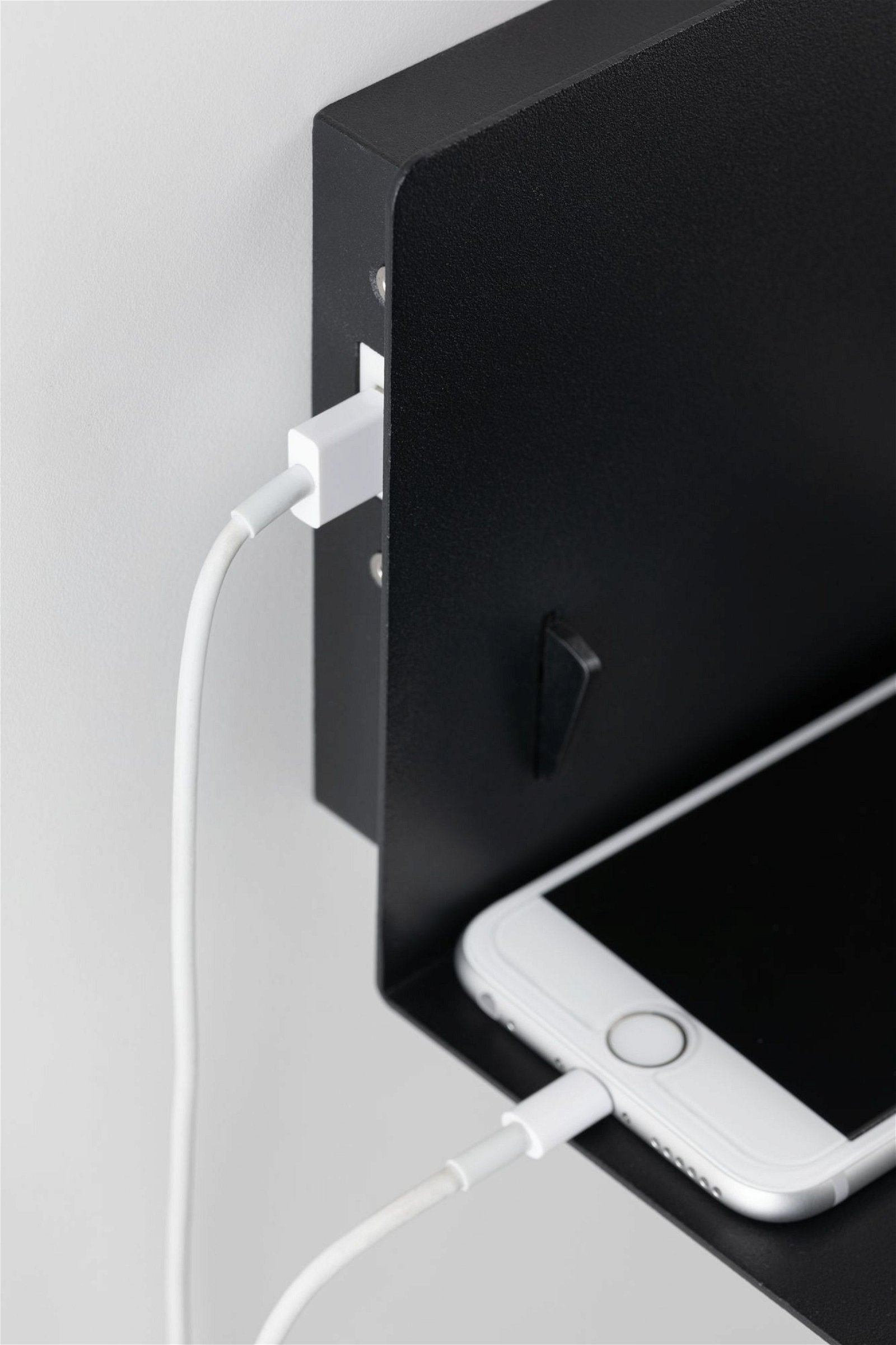 Weißes Telefon, das auf einem schwarzen Regal an einer weißen Wand geladen wird.