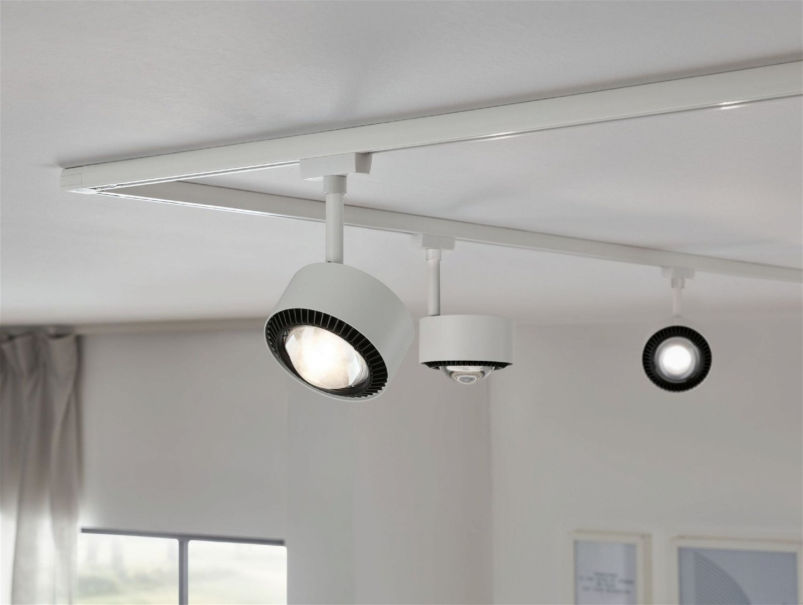 Drei weiße Strahler auf einer Schiene, die einen Raum beleuchten. Die Lichter sind an.