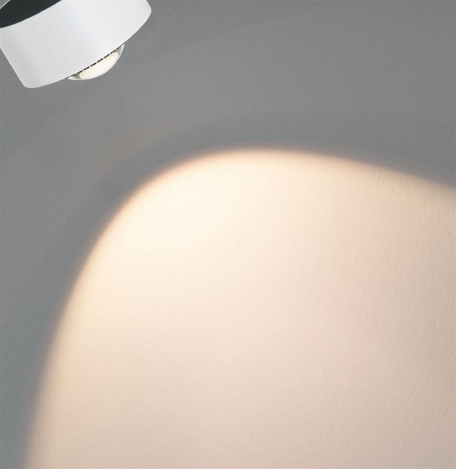 Helles Licht eines Deckenstrahlers an einer grauen Wand.