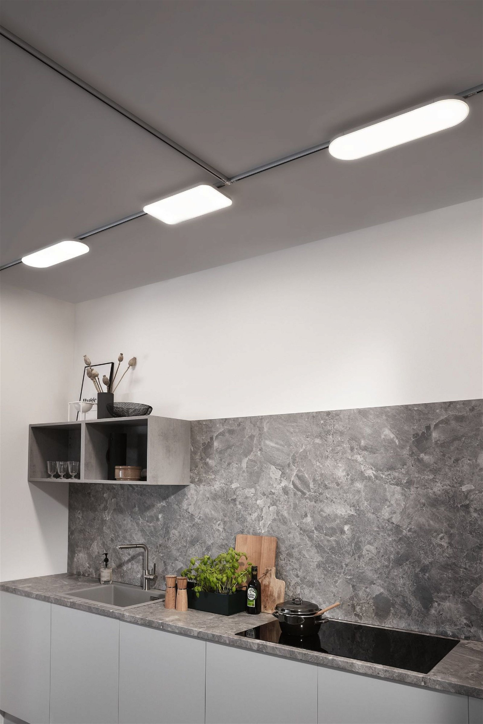 Küche mit grauem Marmorrückwand, Schränken und Schienenbeleuchtung. Theke hat Kochutensilien.