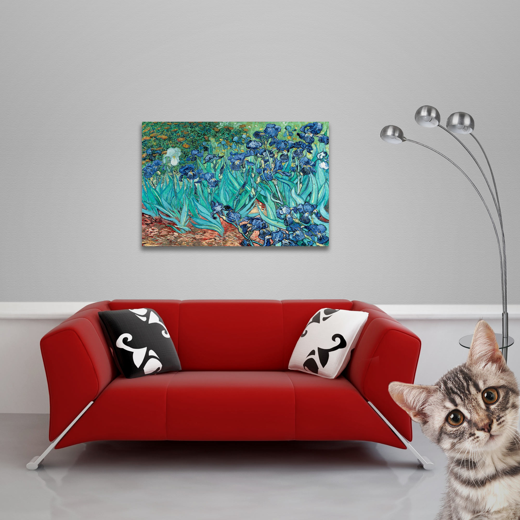 Ein rotes Sofa mit Kissen befindet sich unter einem Gemälde mit blauen Blumen. Eine Katze schaut in die Kamera.