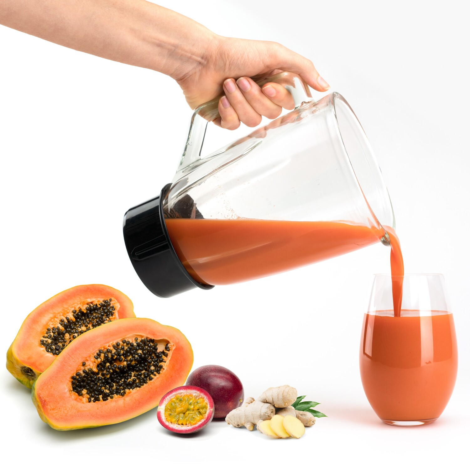 Mano vertiendo jugo de naranja en un vaso. Hay papaya, maracuyá y jengibre.