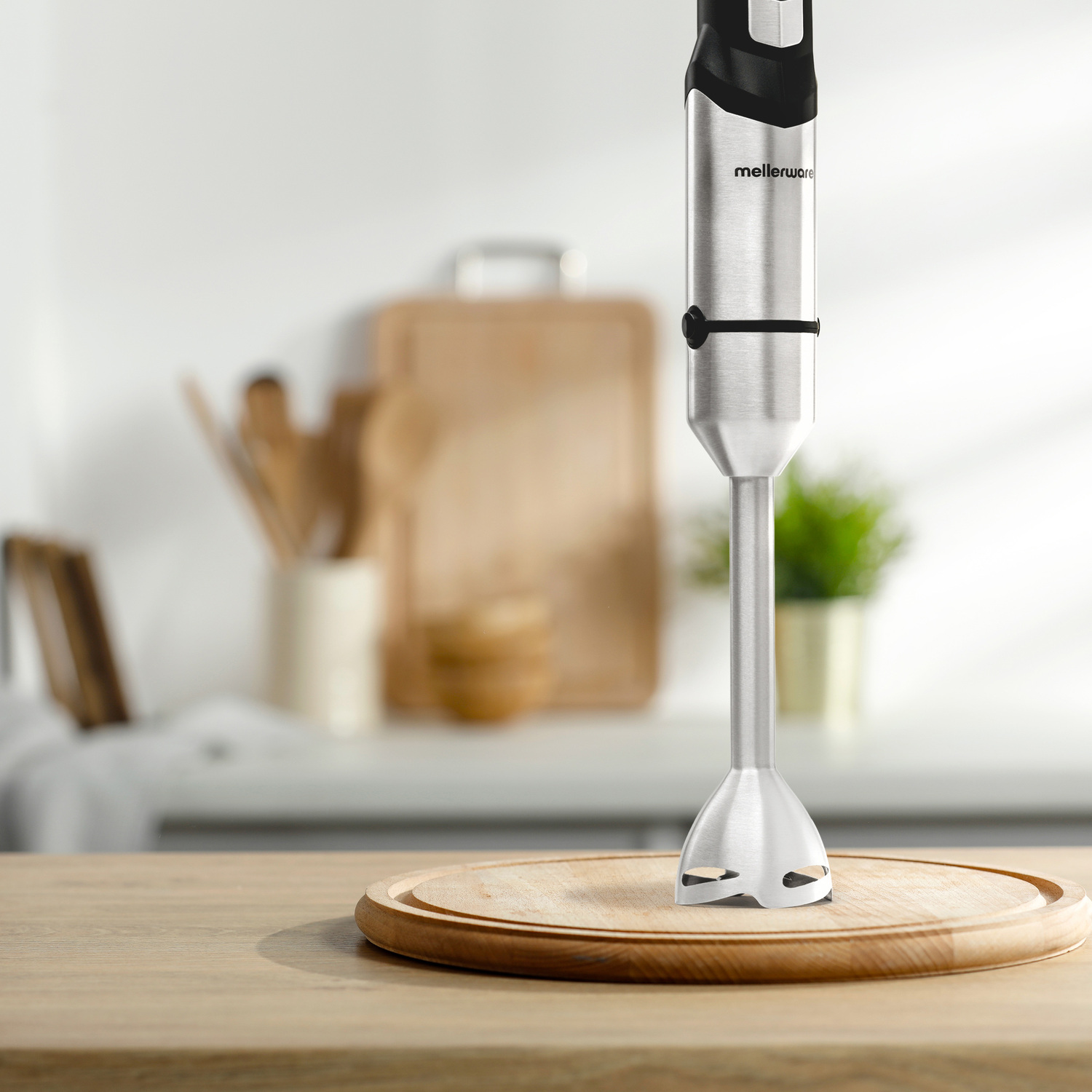 Un frullatore a immersione in acciaio inox è su un tagliere di legno in cucina.