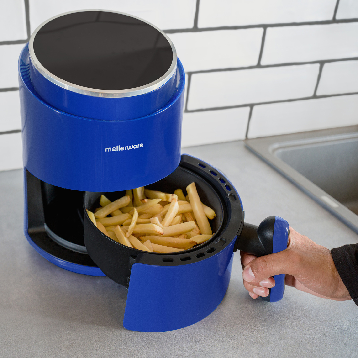 Una friggitrice ad aria blu, con un cestello di patatine fritte rimosso con una mano, su un bancone grigio.