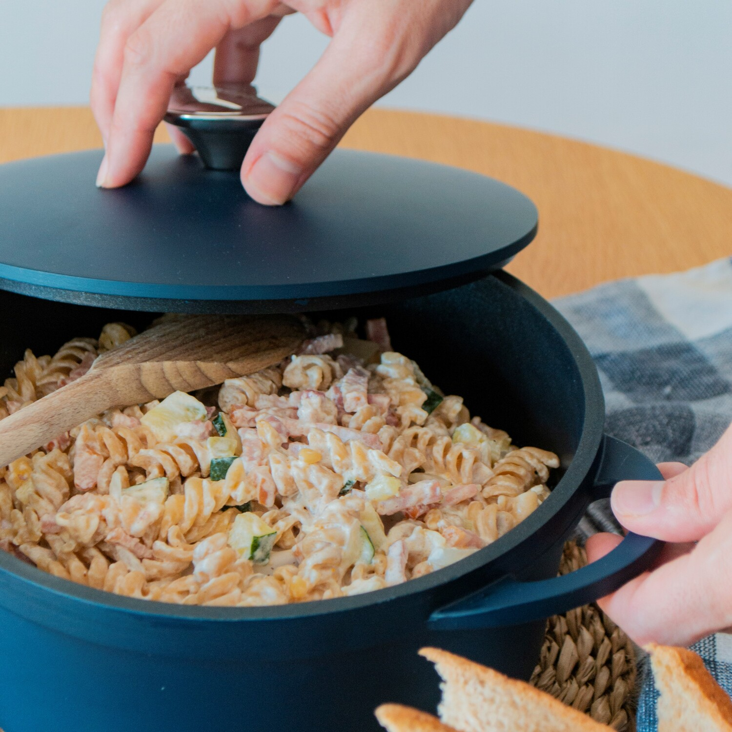 Persona abriendo una olla de pasta. Pasta con verduras y carne es visible.