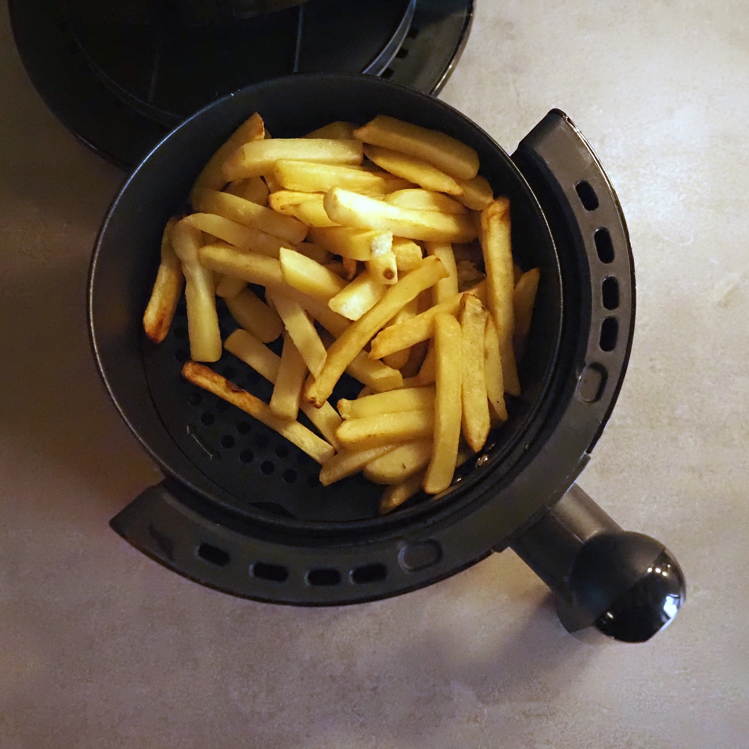 Patatine fritte fresche in un cestello per friggitrice ad aria nero, vista da vicino.
