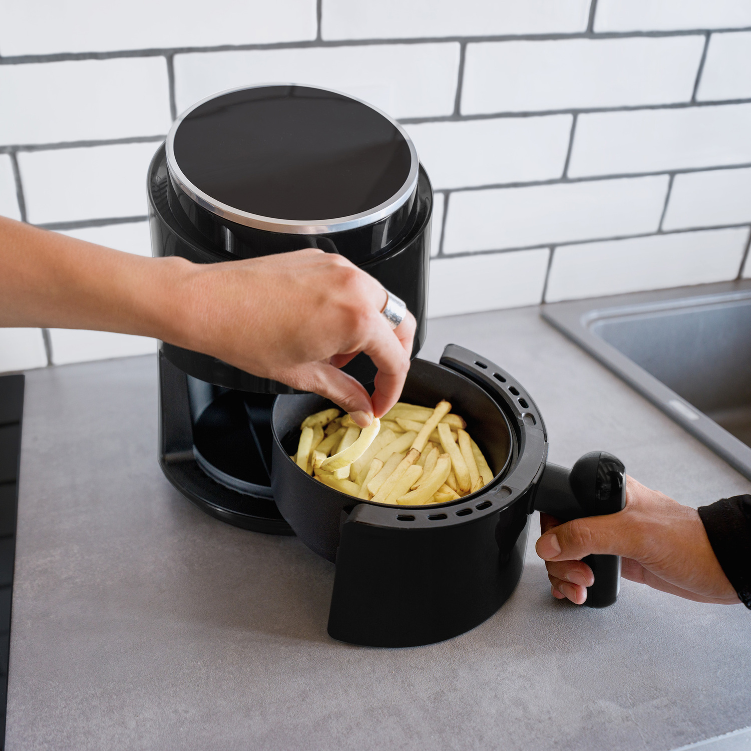 Una persona sta mettendo patatine fritte in una friggitrice ad aria nera. Ambiente cucina.