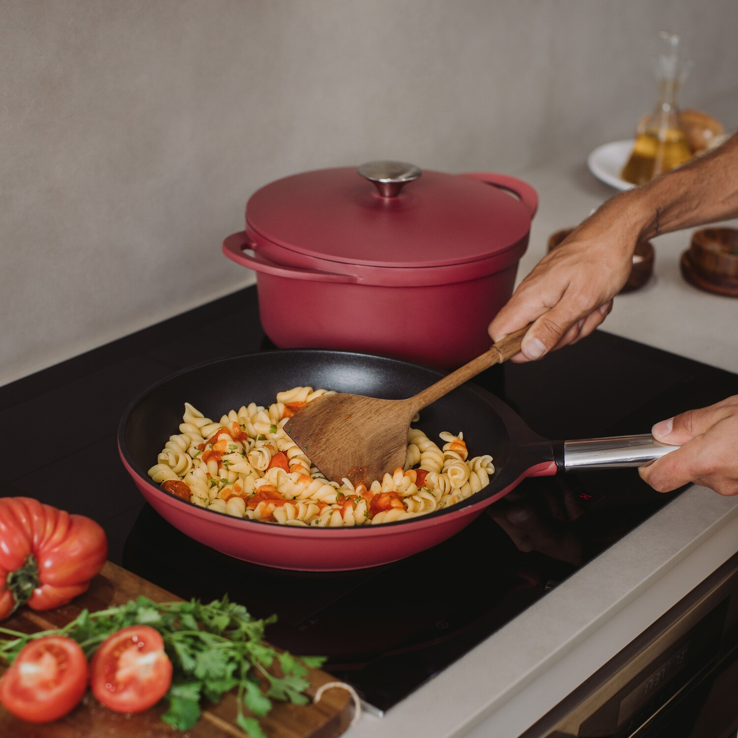 Hombre cocinando pasta en una sartén. Olla roja, tomates y otros ingredientes en la mesa.