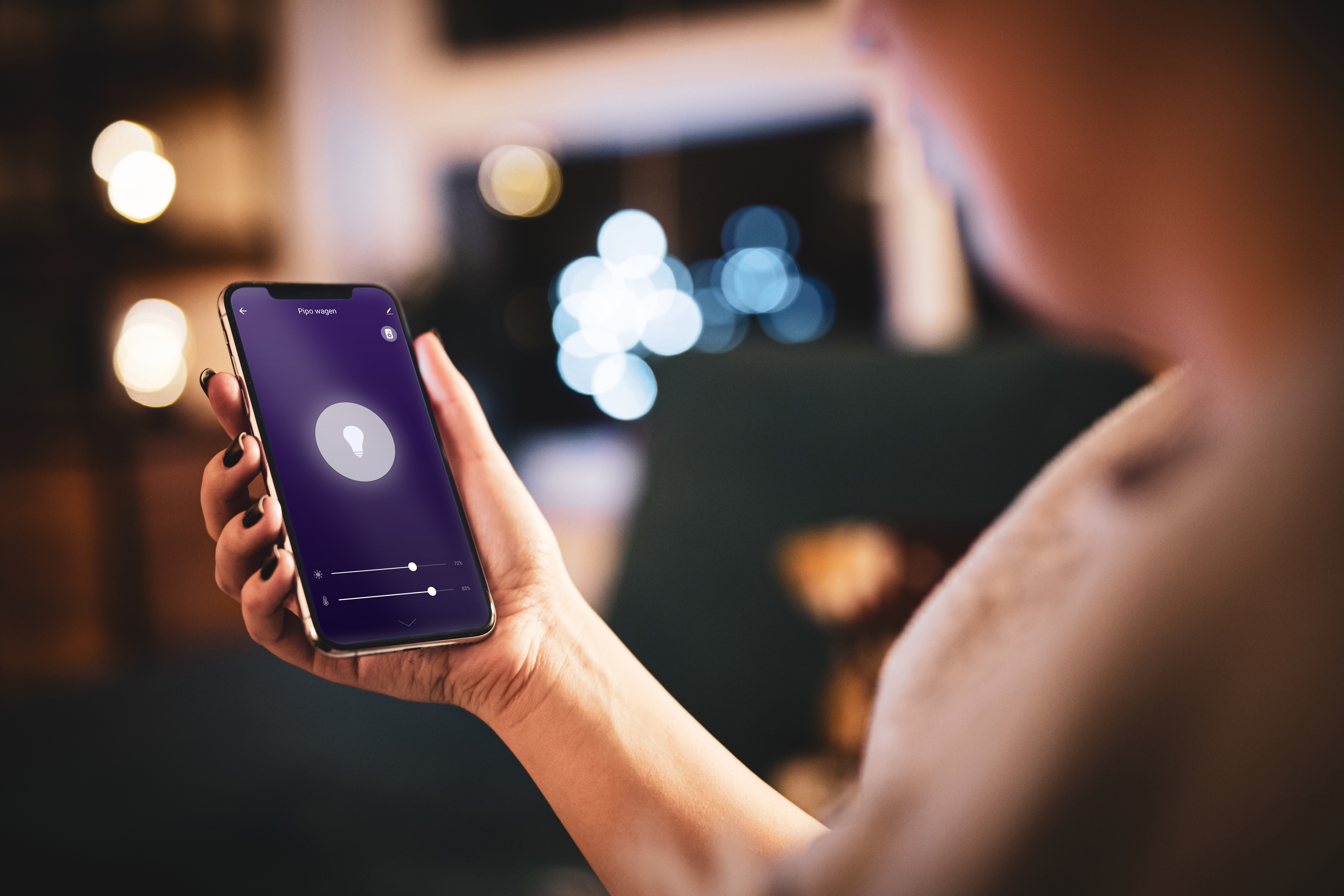 Osoba trzymająca smartfon z ekranem wyświetlającym ikonę żarówki i suwaki regulacji.