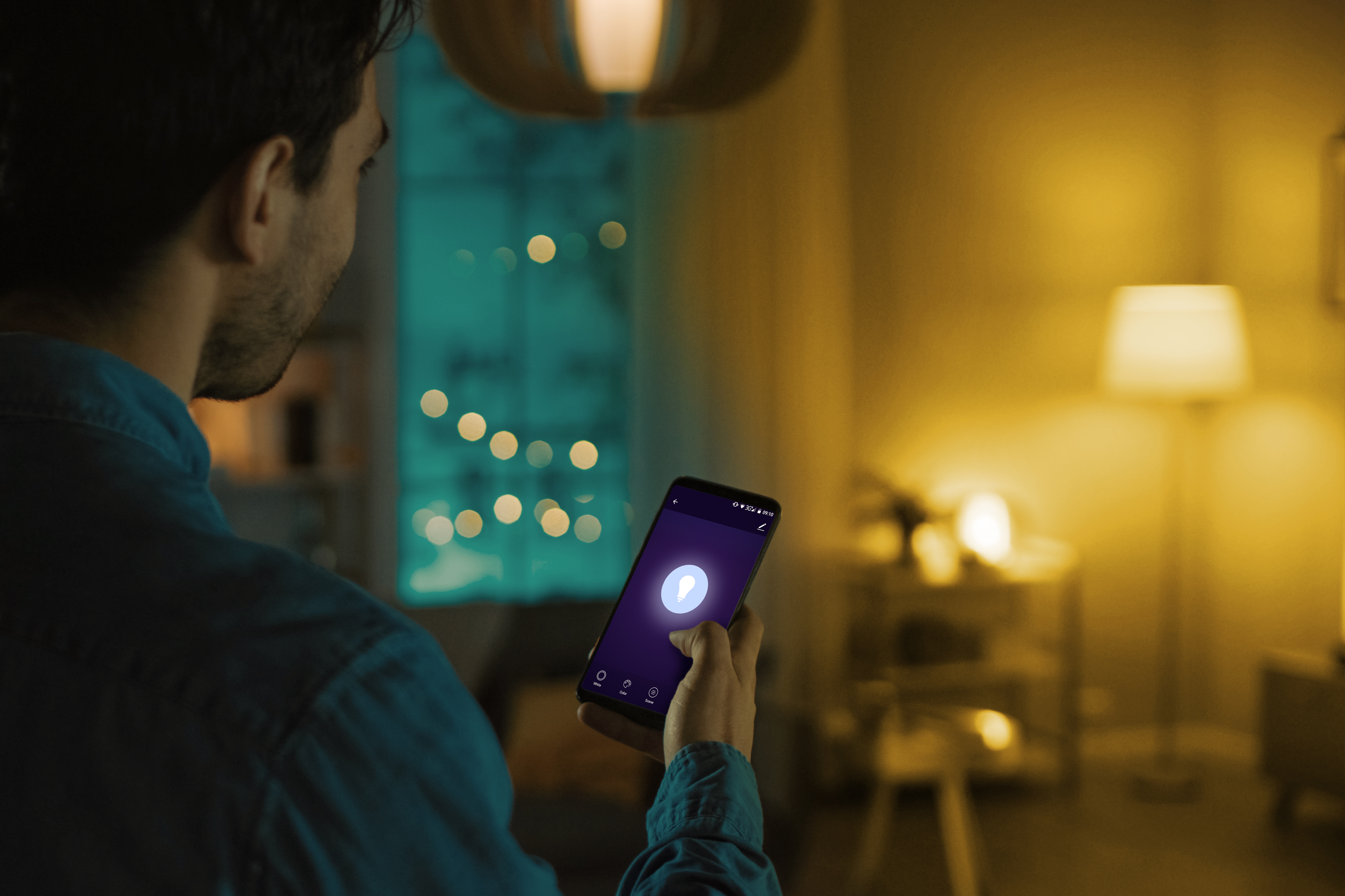 Mężczyzna używa smartfona w pokoju oświetlonym światłem otoczenia. Telefon pokazuje ikonę żarówki.