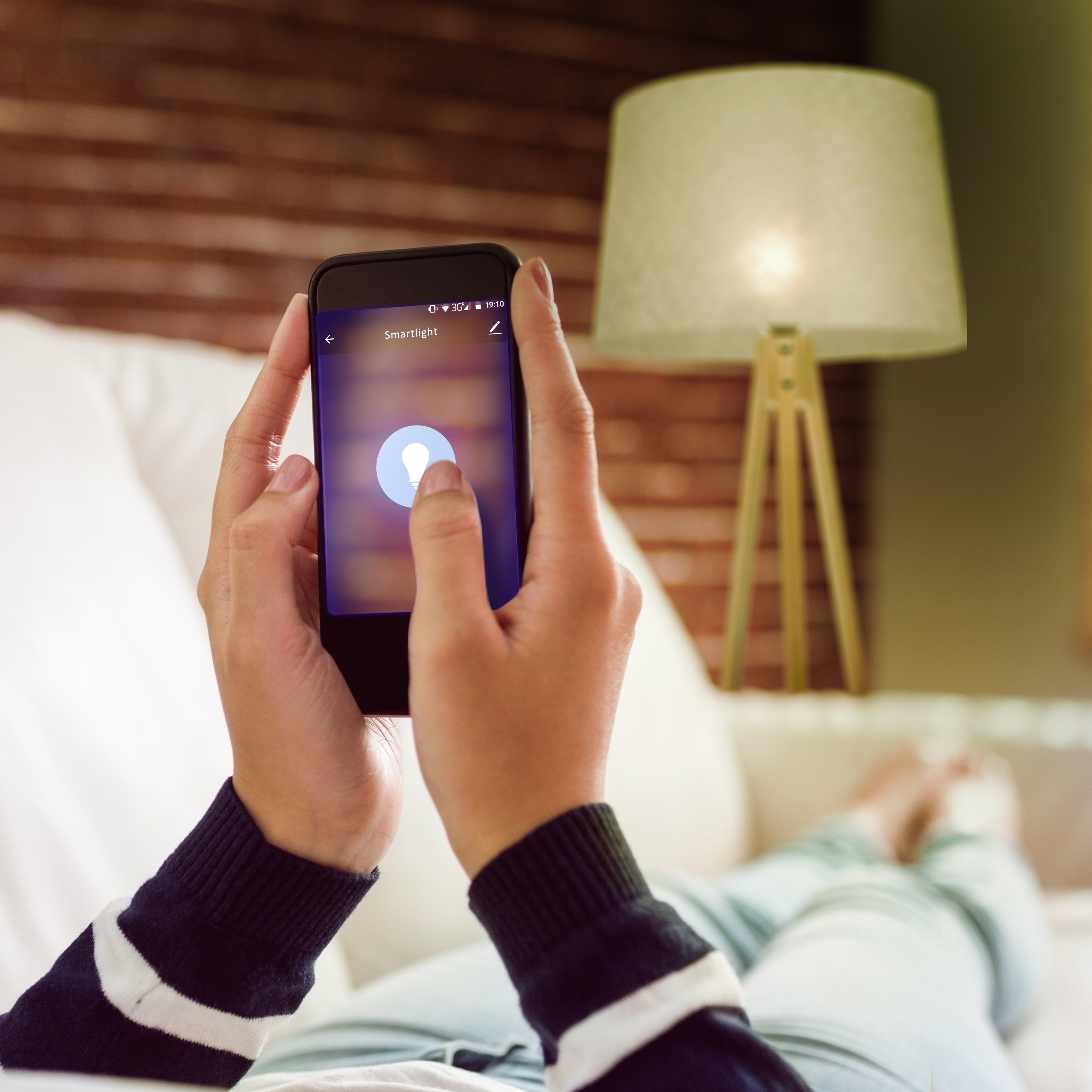 Dłonie trzymające telefon z aplikacją inteligentnego oświetlenia, z lampą w tle.