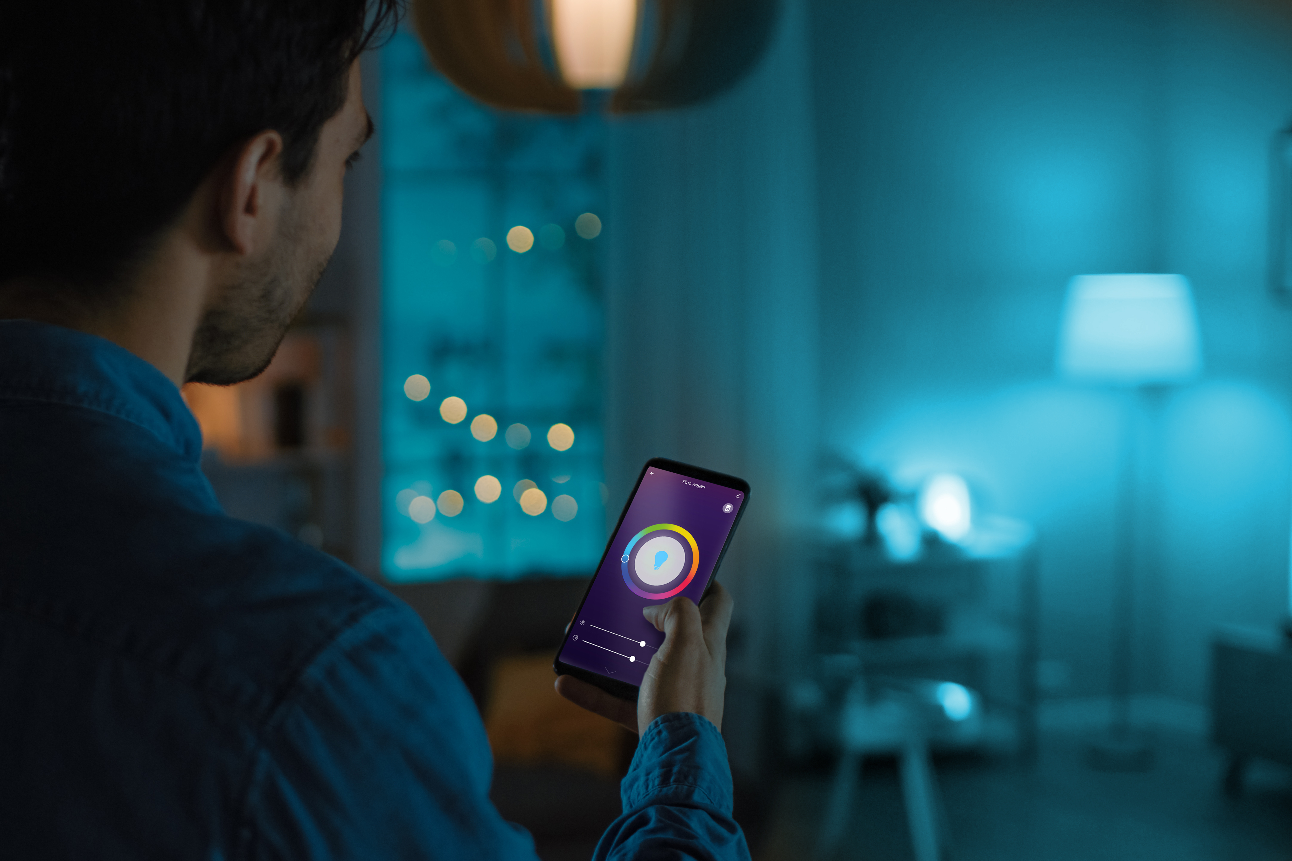 Mężczyzna trzyma smartfona z interfejsem kontroli koloru. Pokój jest oświetlony na niebiesko.