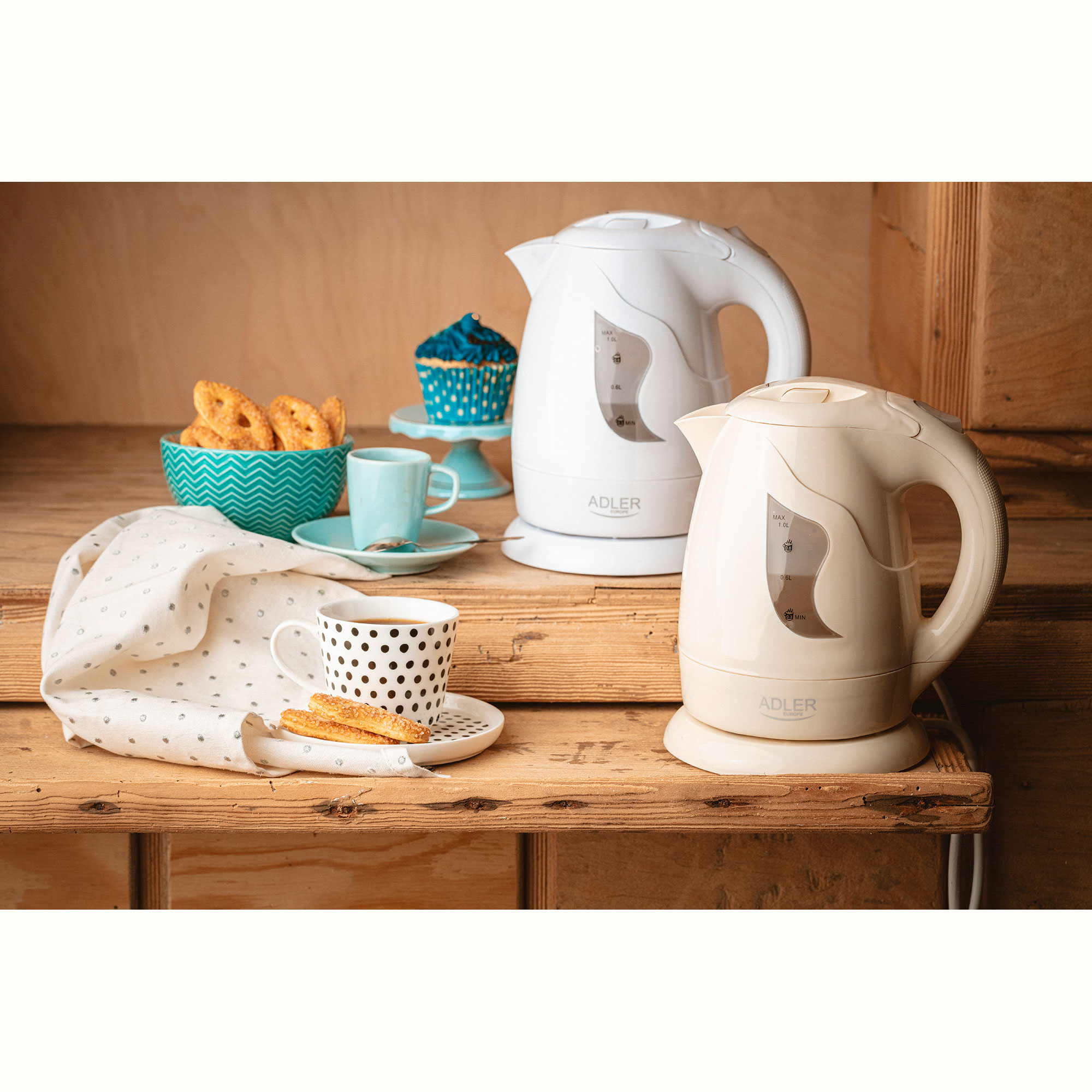 Dwa białe czajniki elektryczne, filiżanka, spodek i mała miseczka ciasteczek na drewnianym stole.