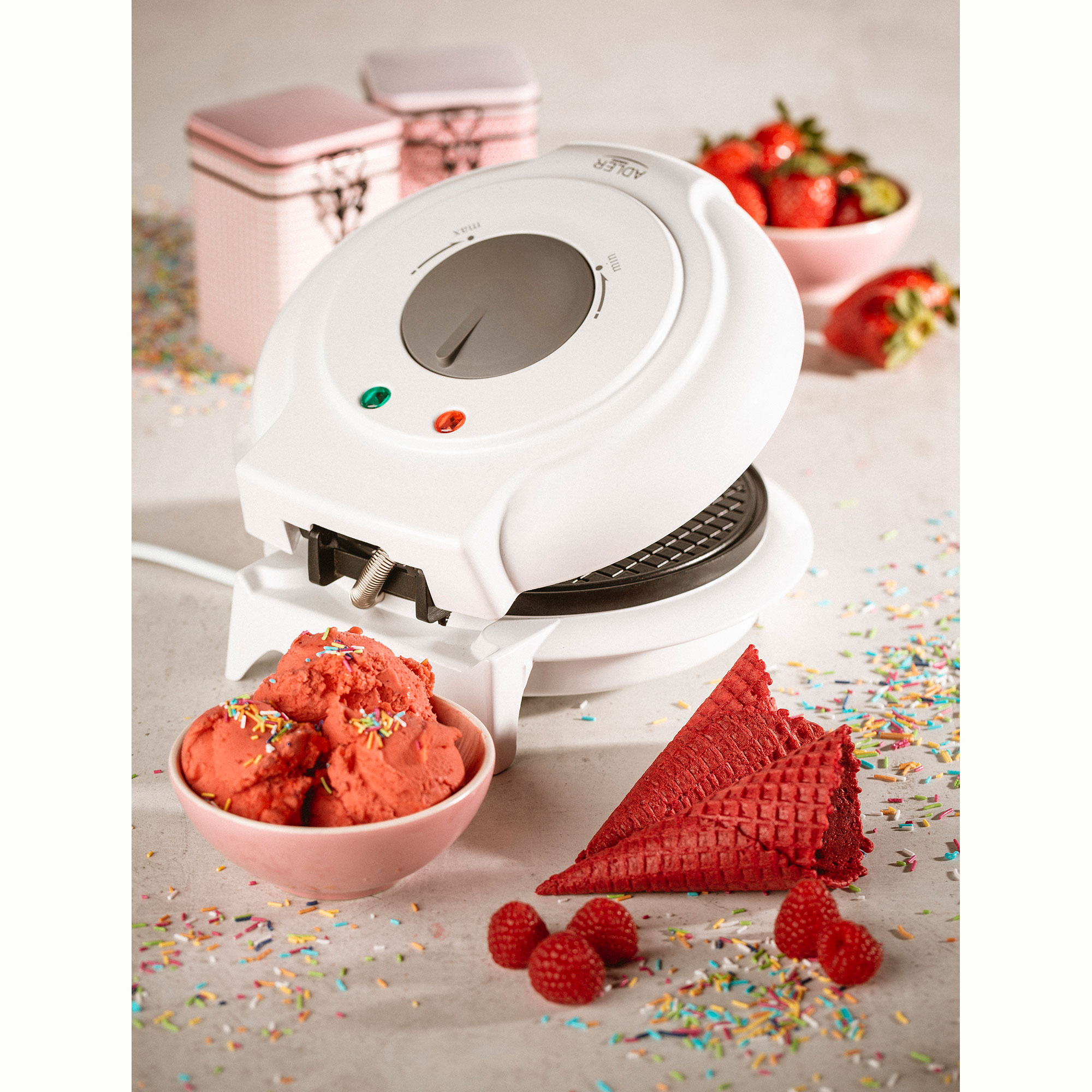 White waffle maker, waffles, and toppings, with raspberries and sprinkles.