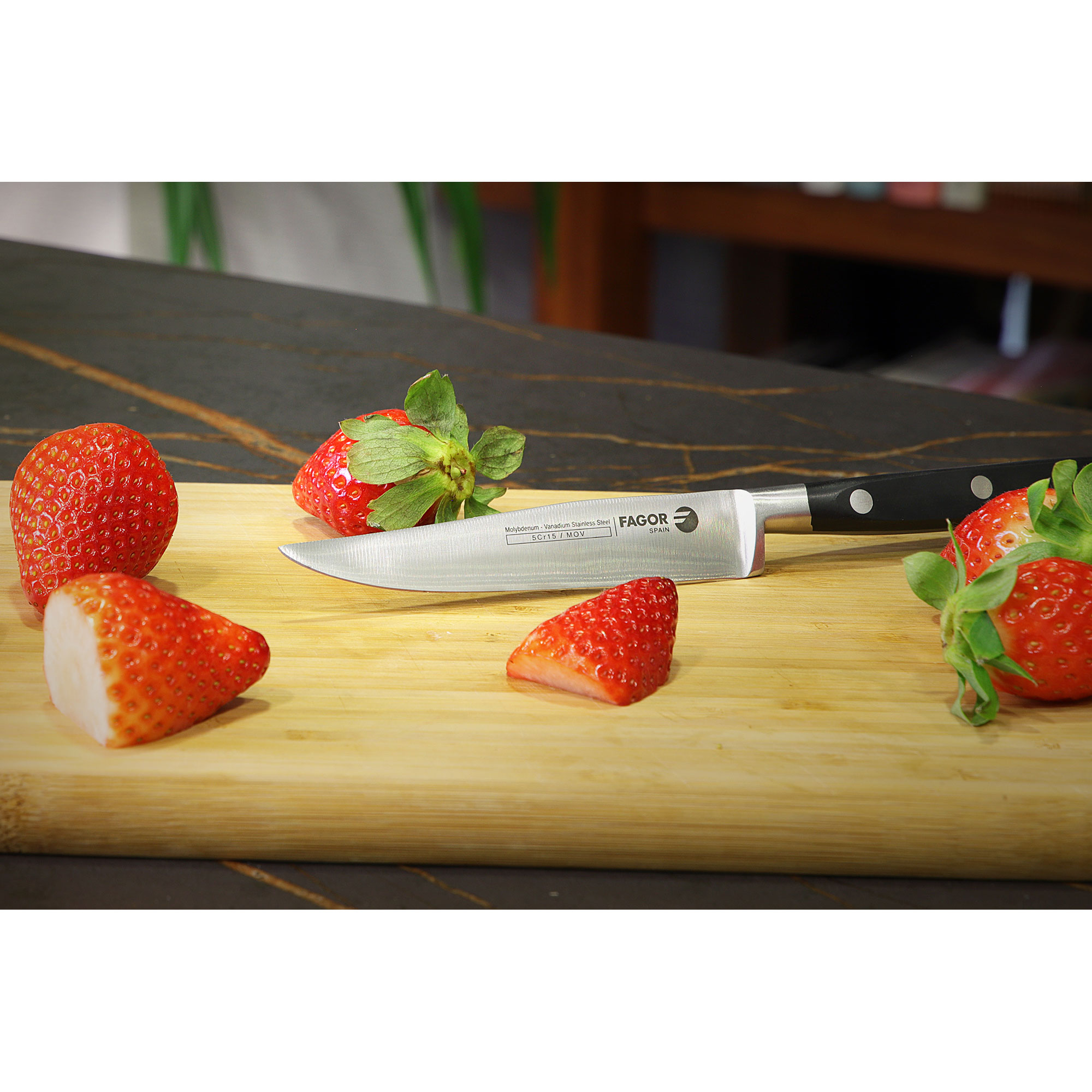 Cuchillo y fresas en una tabla de cortar de madera, fondo de encimera negra.