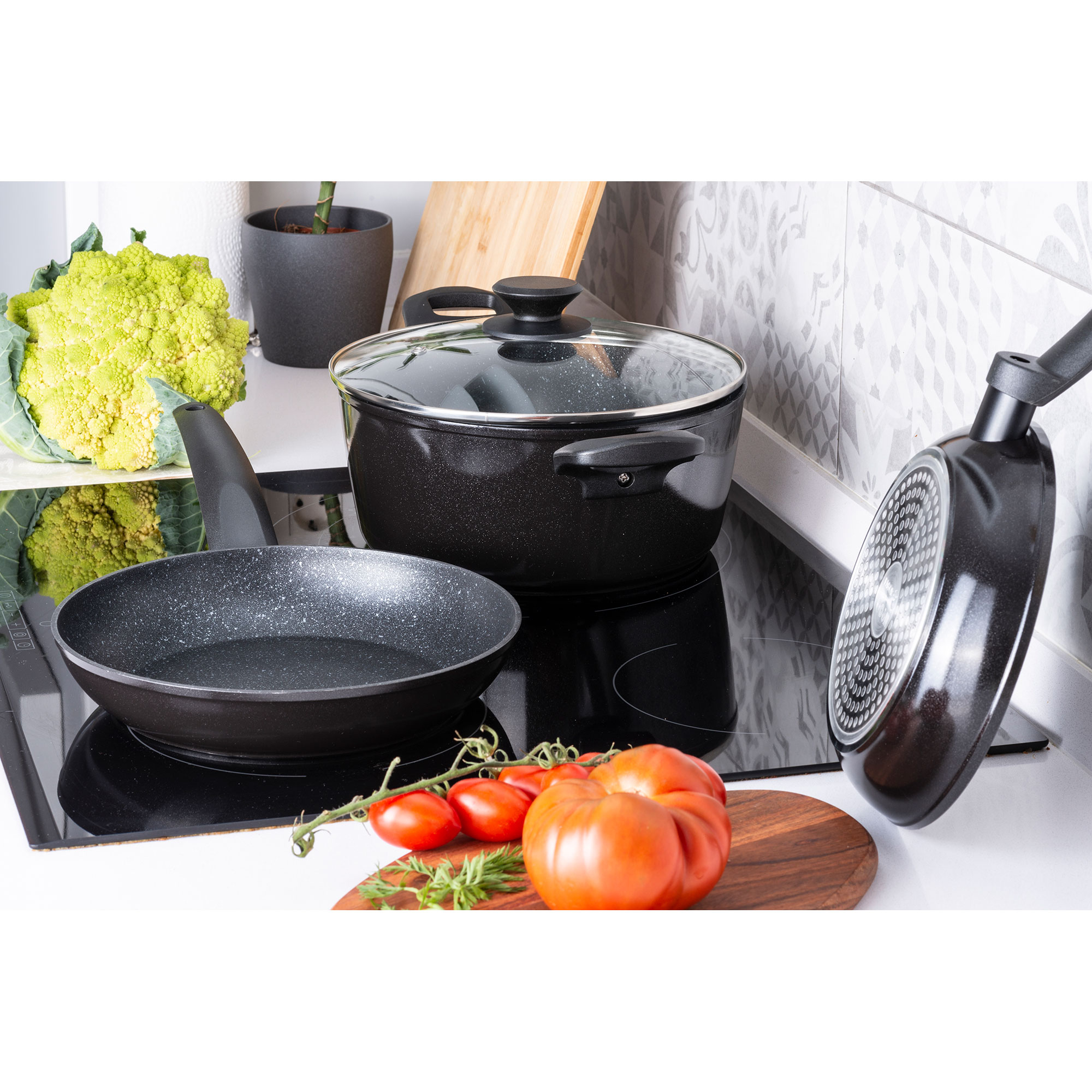 Encimera de cocina con utensilios de cocina, tomates y productos frescos. Una encimera negra.