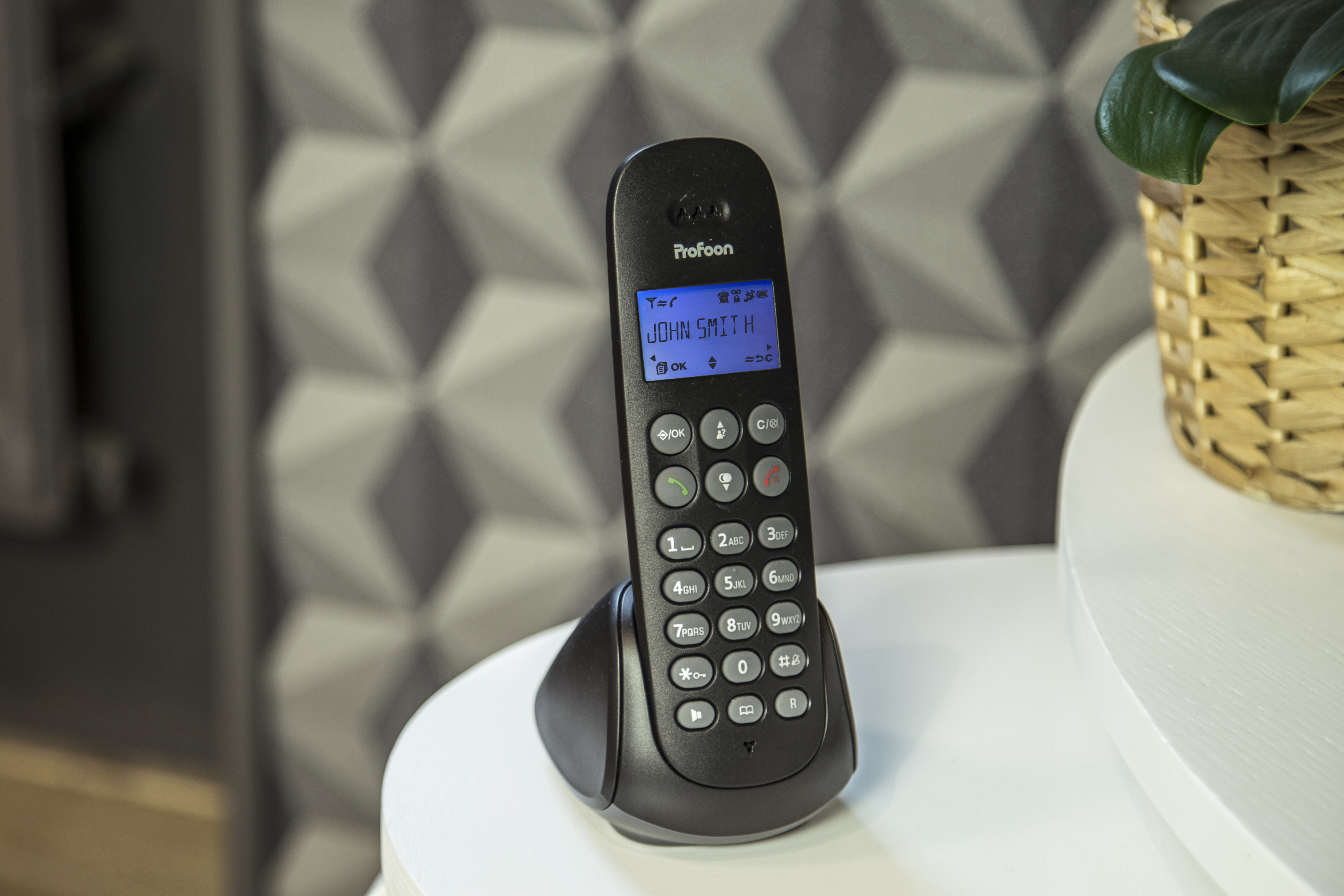 Ein schwarzes schnurloses Telefon auf einem weißen Tisch, zeigt einen Bildschirm mit Text.