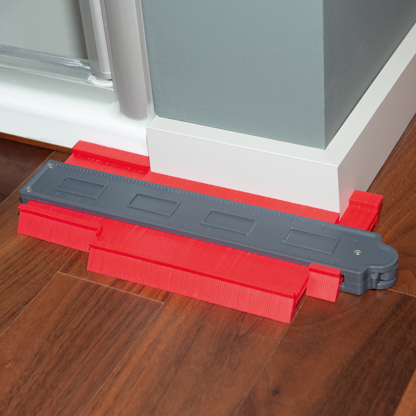 Rotes und graues Konturmesswerkzeug auf Holzboden, weiße Wand und graue Ecke.