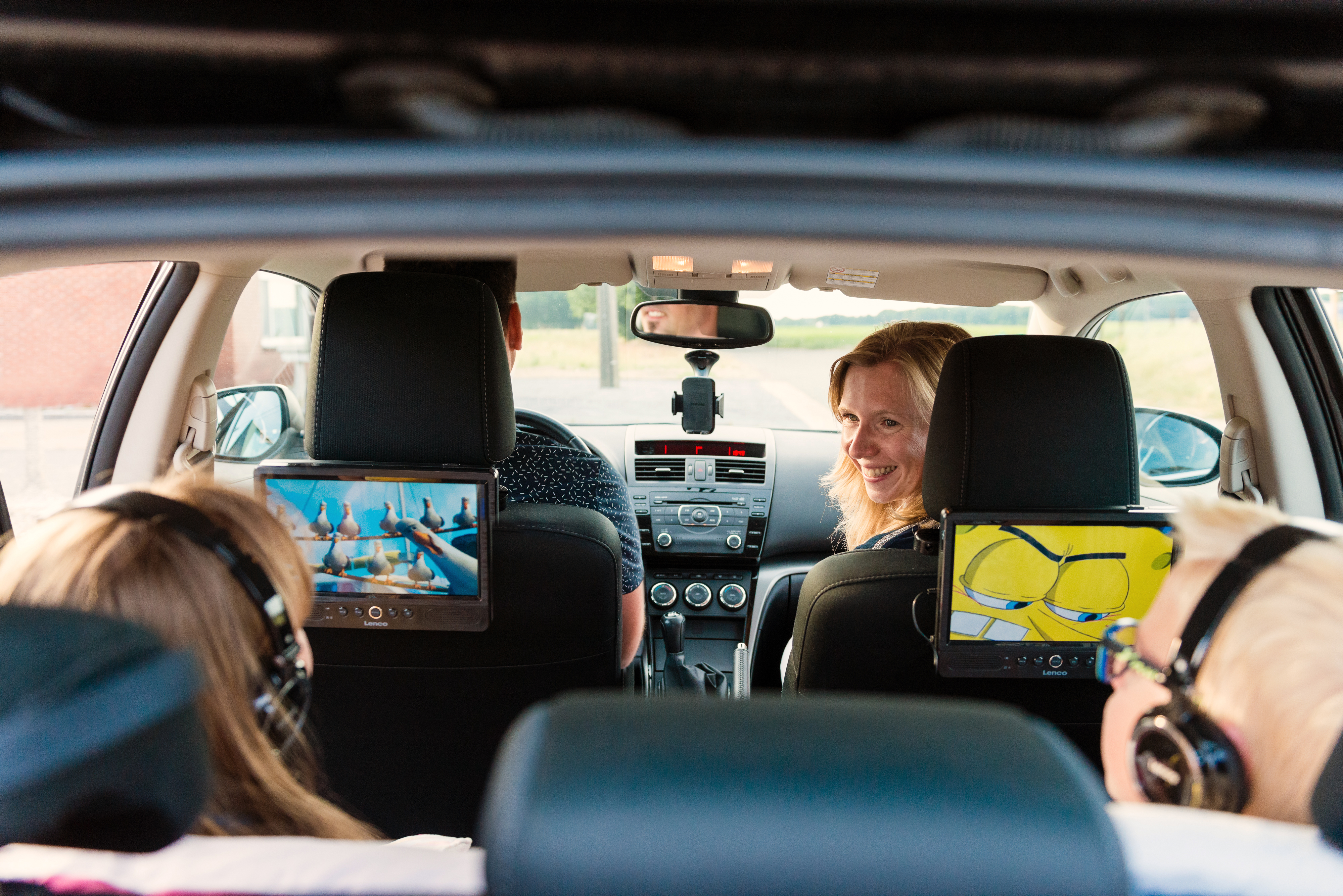 Im Auto spielen zwei Bildschirme Cartoons. Personen auf Vordersitzen sind sichtbar.