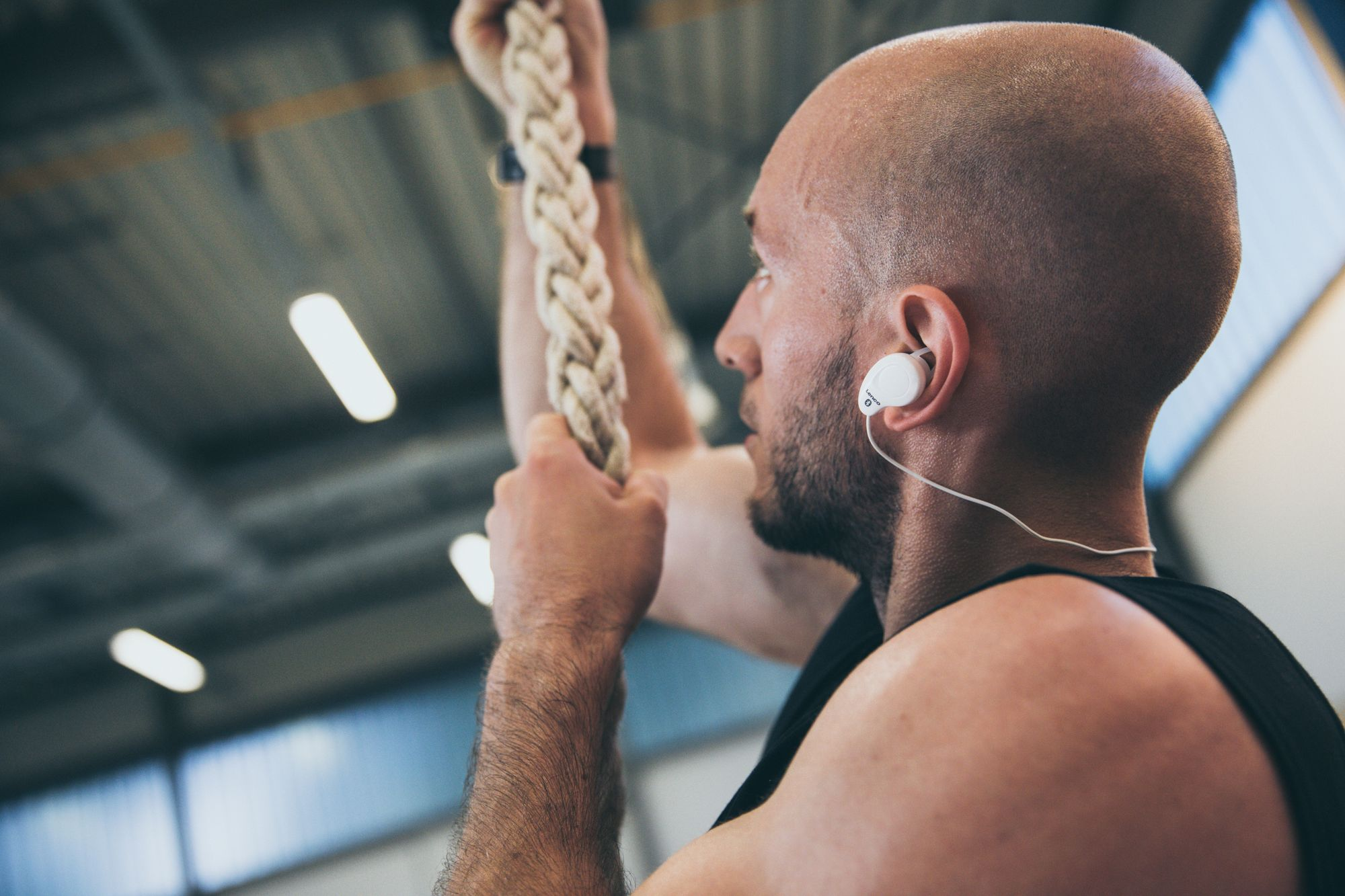 Glatzköpfiger Mann mit Ohrhörern, der ein Seil hält, im Fitnessstudio.