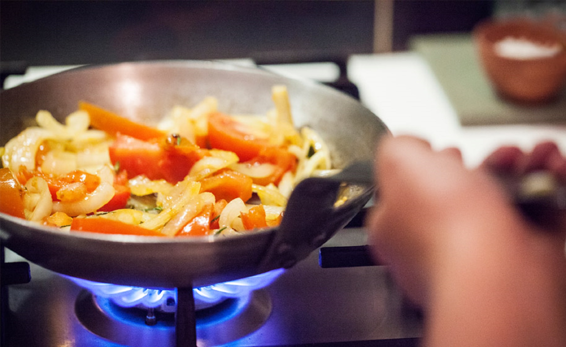 Cocinando en una sartén. Tomates y cebollas en una sartén sobre llama azul.