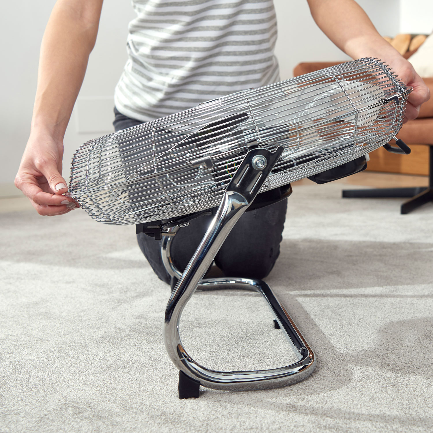 Una persona è in ginocchio, che assembla un ventilatore argentato in stile retrò su un pavimento in moquette.