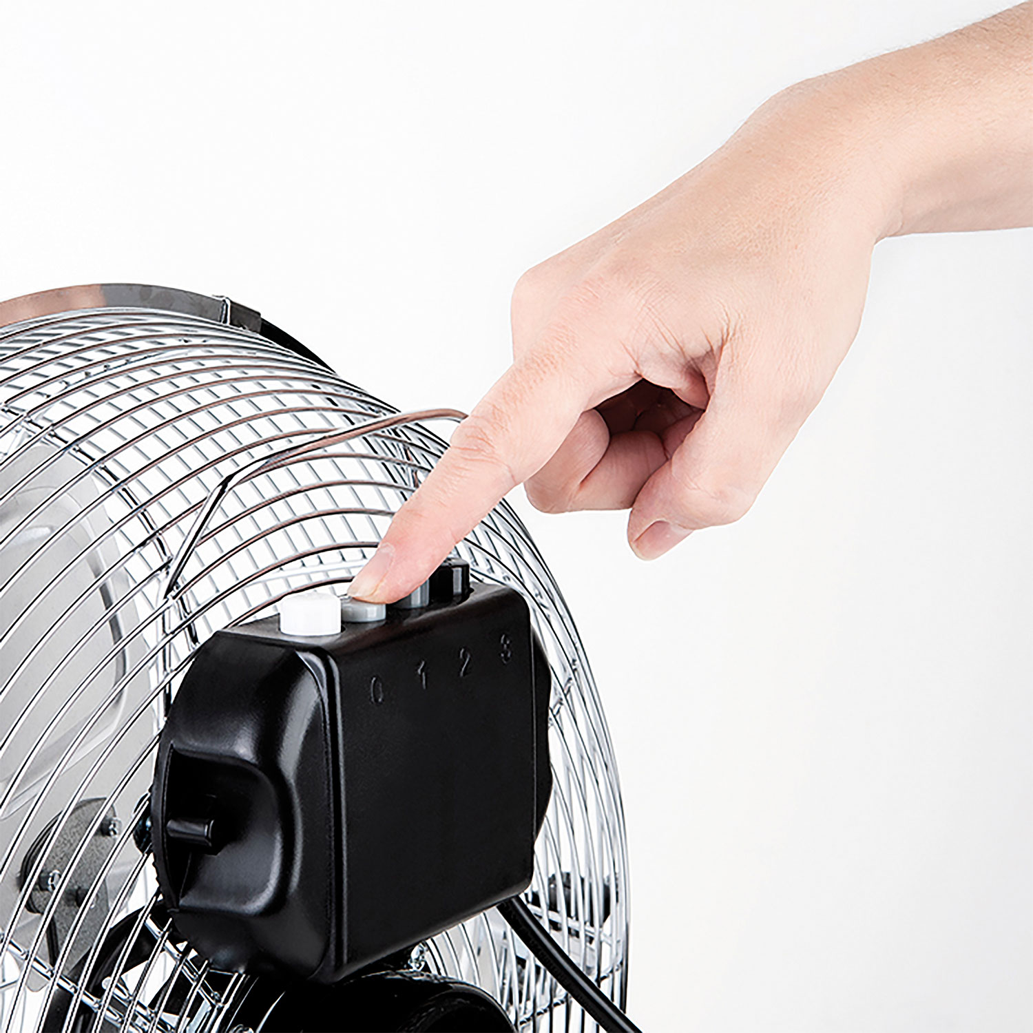 Una mano preme un pulsante su un ventilatore con una gabbia di metallo, pannello di controllo numerato, sfondo bianco.