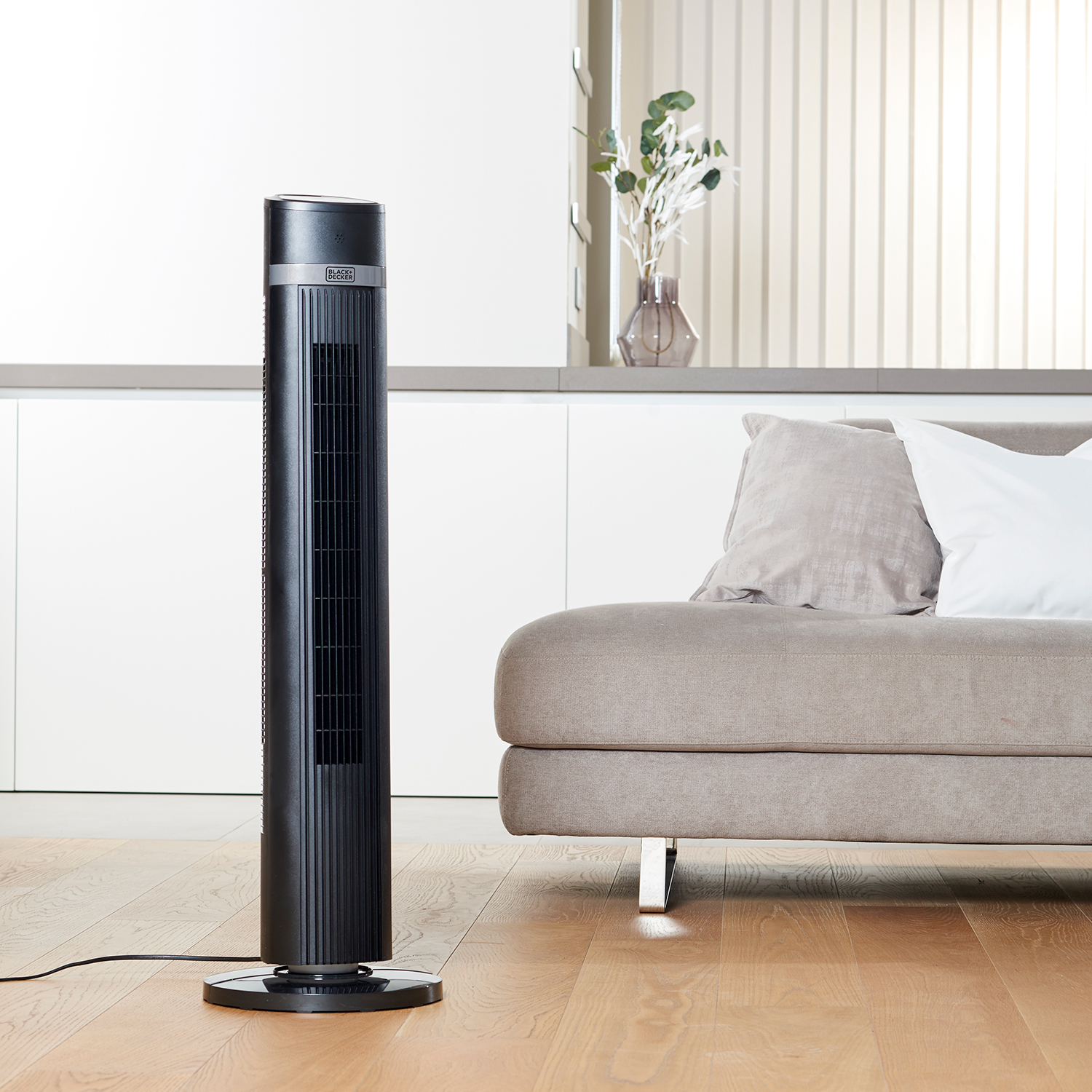 Un ventilador de torre negro junto a un sofá en un salón moderno.