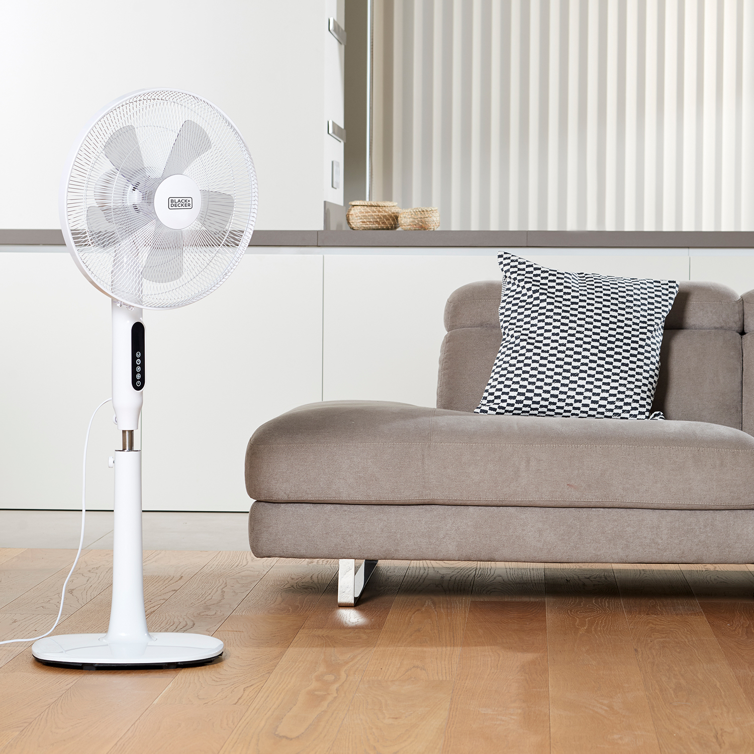 Un ventilatore a colonna bianco, divano e cuscino, su un pavimento in legno. Interno.