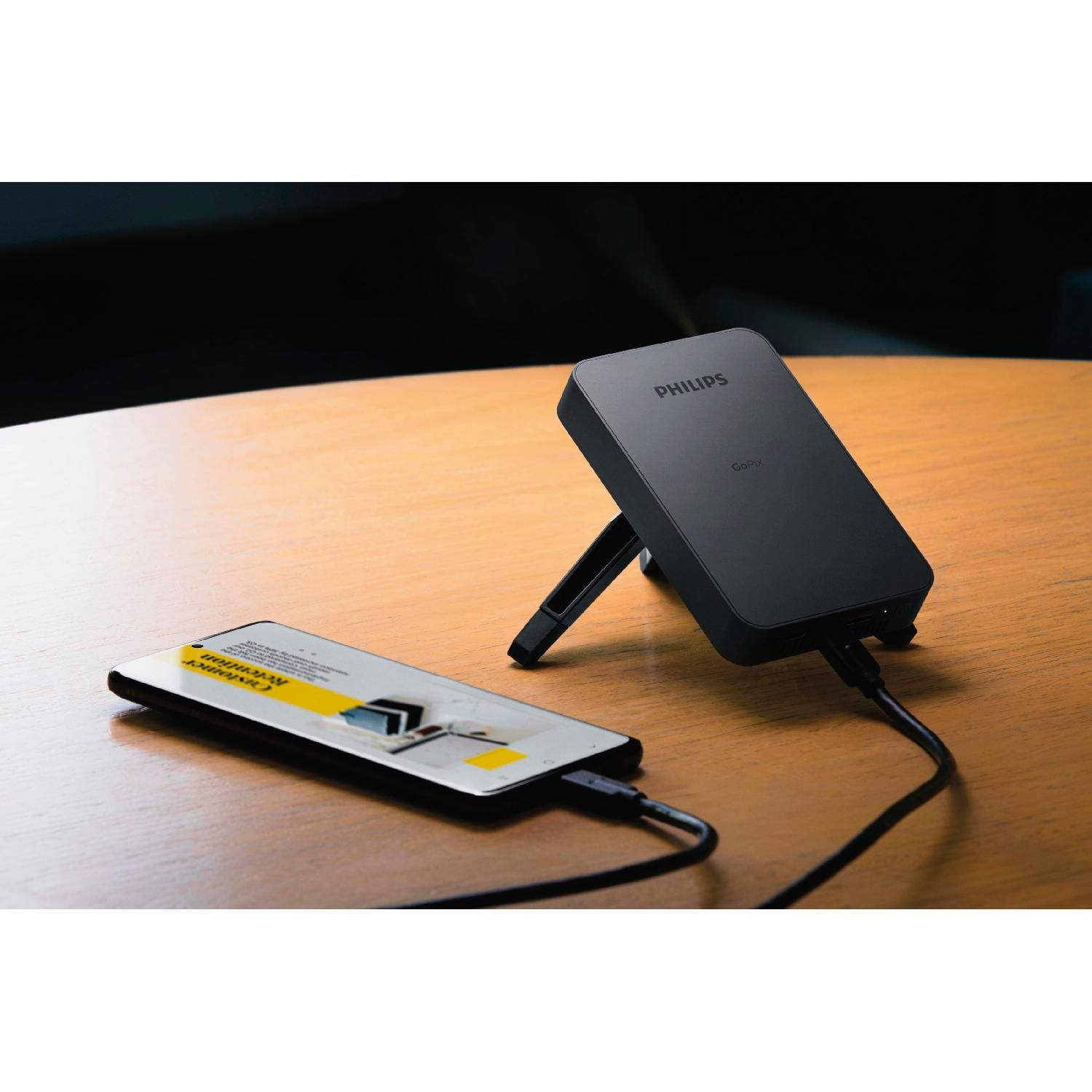 Un cargador inalámbrico negro con un teléfono encima, conectado al cargador con un cable.