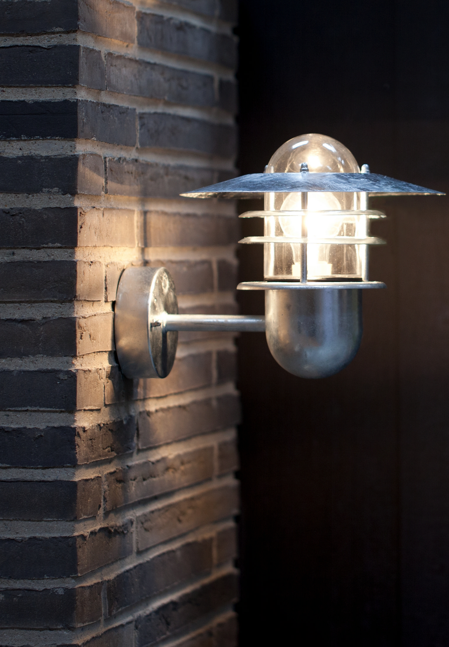 Silberne Außenlampe an einer Backsteinmauer, mit Glasgehäuse und Licht im Inneren.