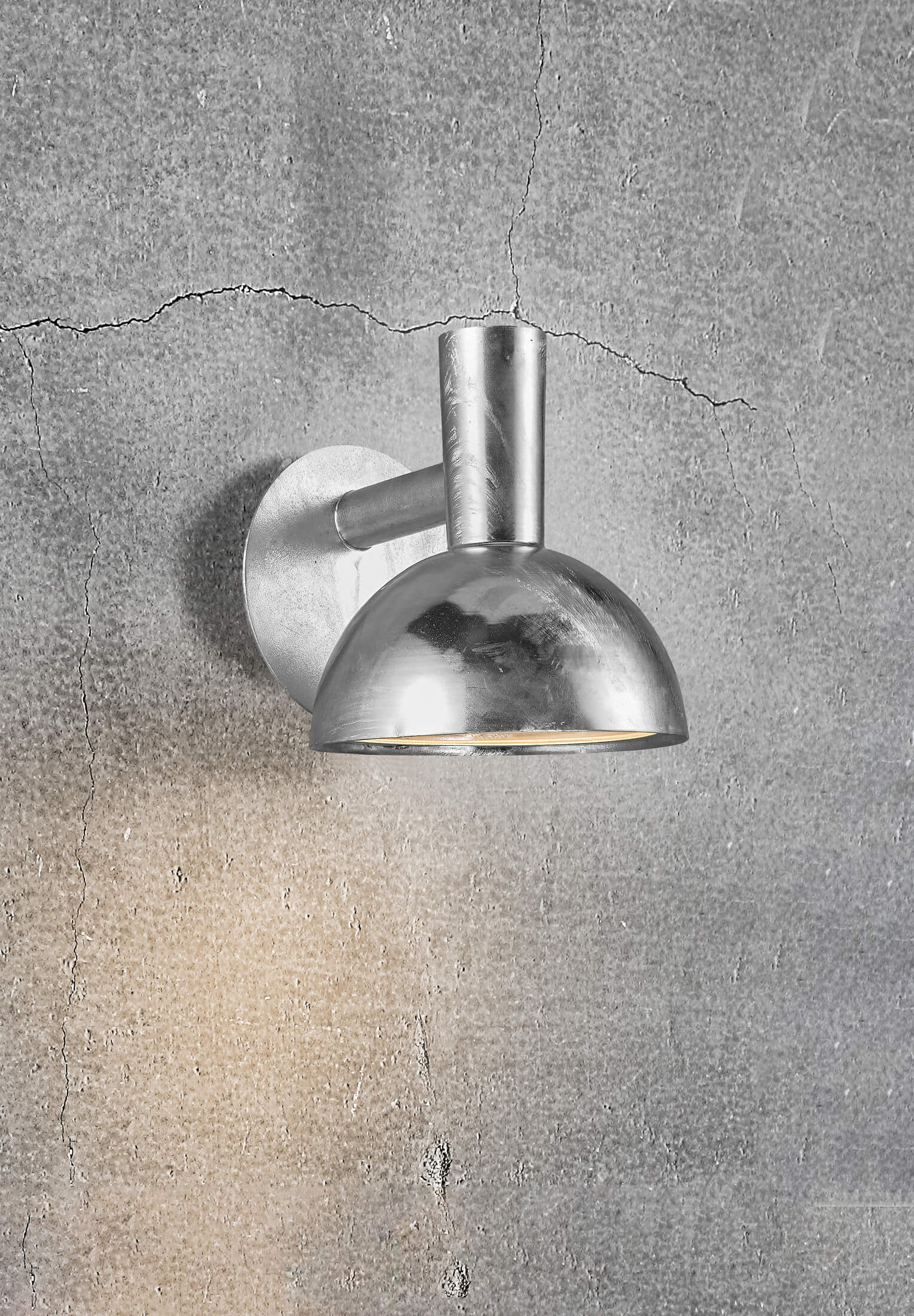 Eine silberne Wandleuchte ist an einer grauen Wand montiert. Die Lampe hat einen abgerundeten Schirm und einen gebogenen Arm.
