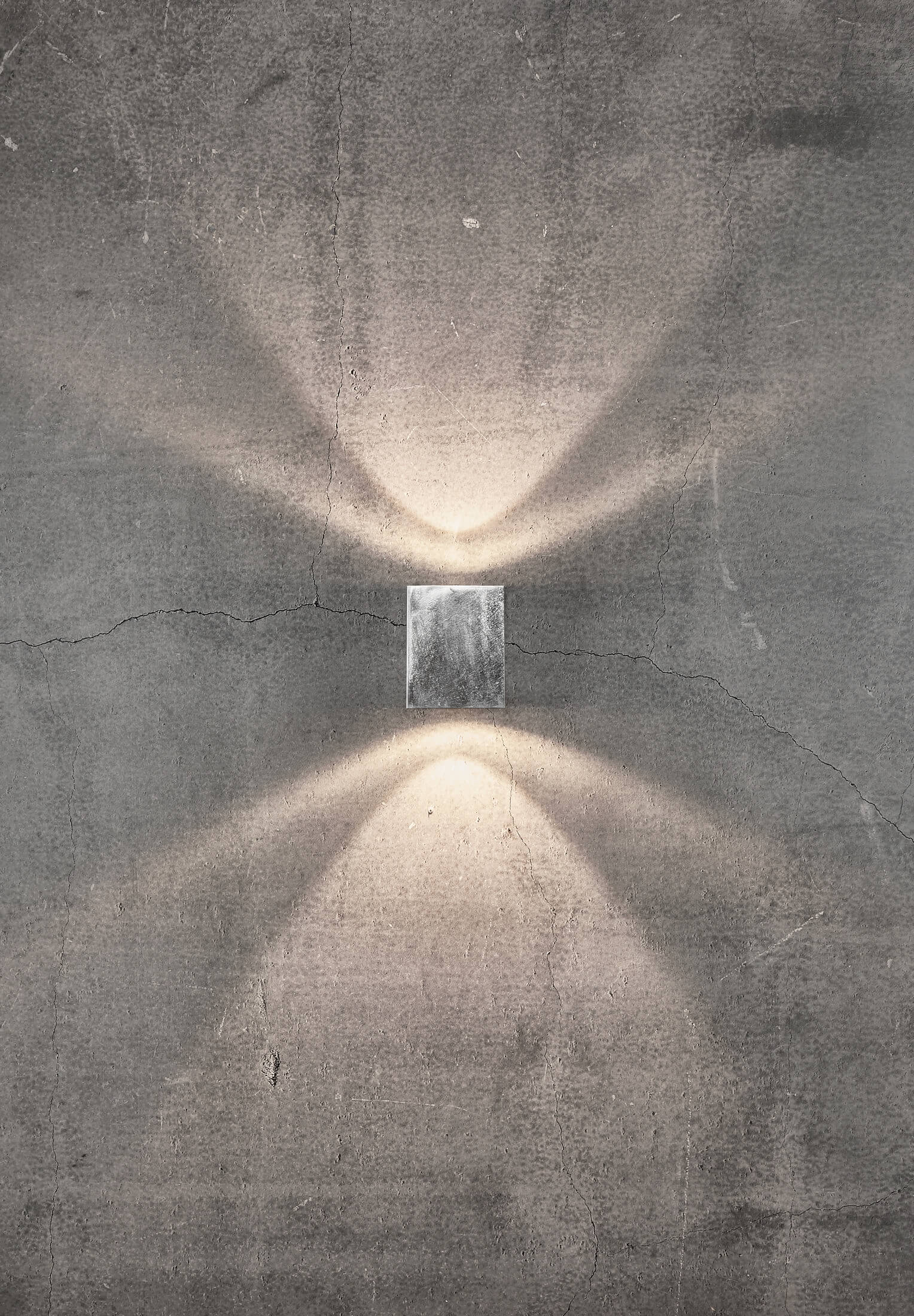 Eine rechteckige Metall-Wandleuchte strahlt zwei Lichtstrahlen auf eine graue Betonwand.