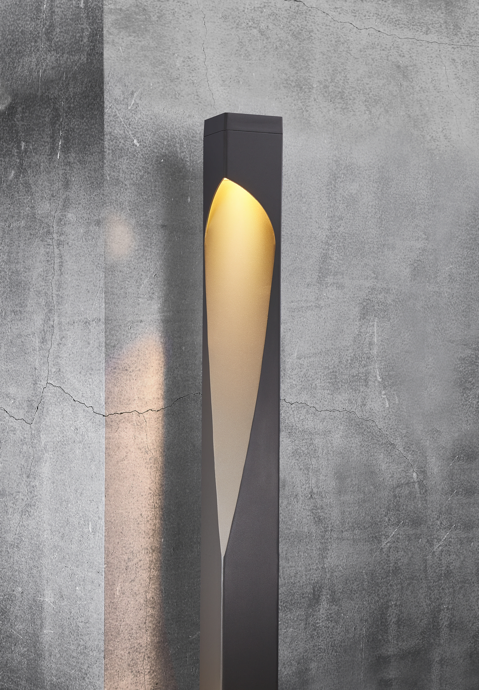 Eine schwarze und goldene Außenlampe steht vor einer grauen, strukturierten Wand.