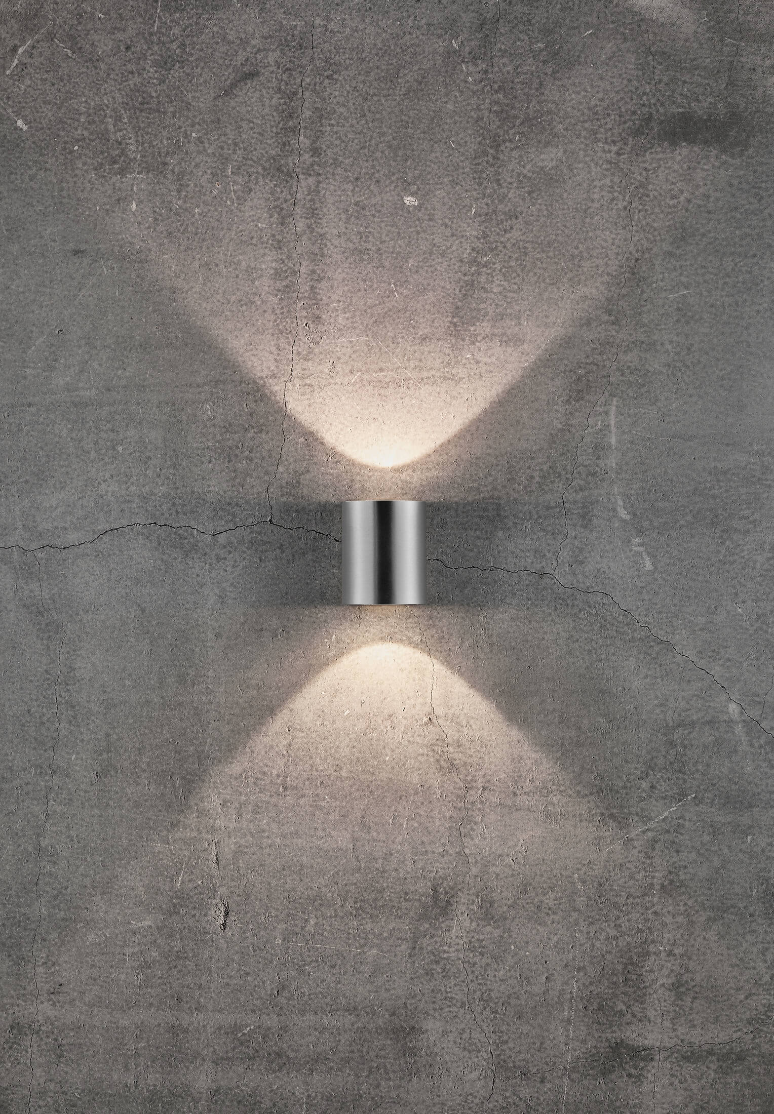 Eine silberne Wandleuchte an einer grauen Betonmauer, mit Lichtstrahlen.