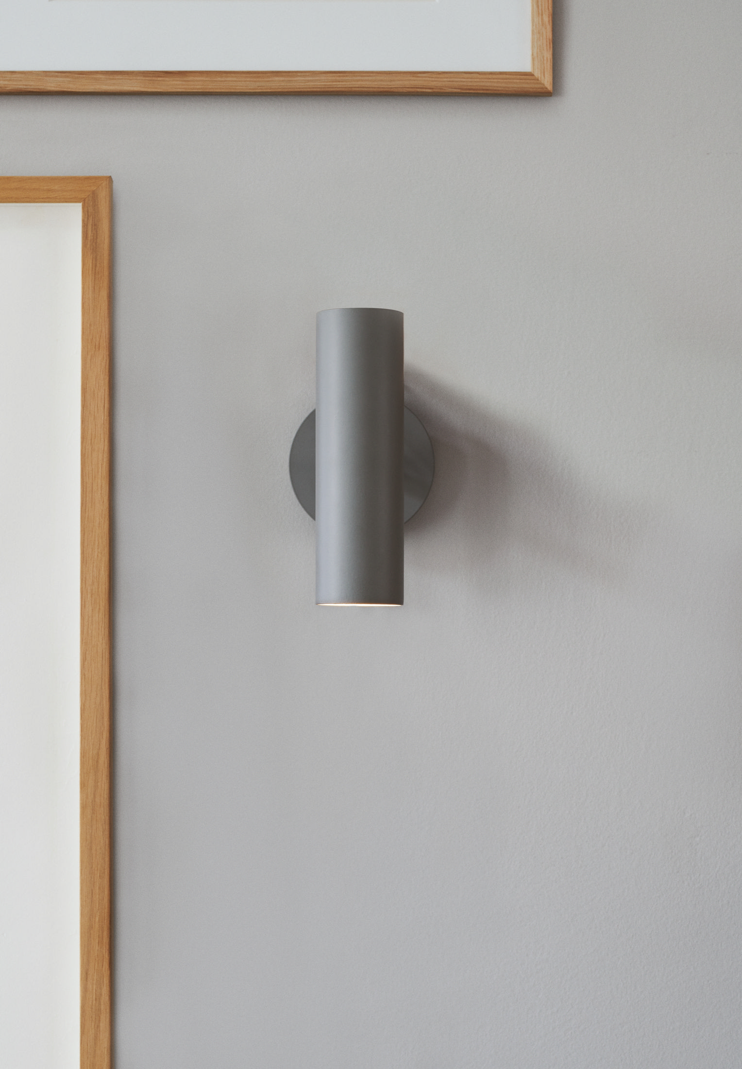 Eine grau an der Wand befestigte Lampe. Sie hat eine zylindrische Form und ist auf einem runden Sockel montiert.