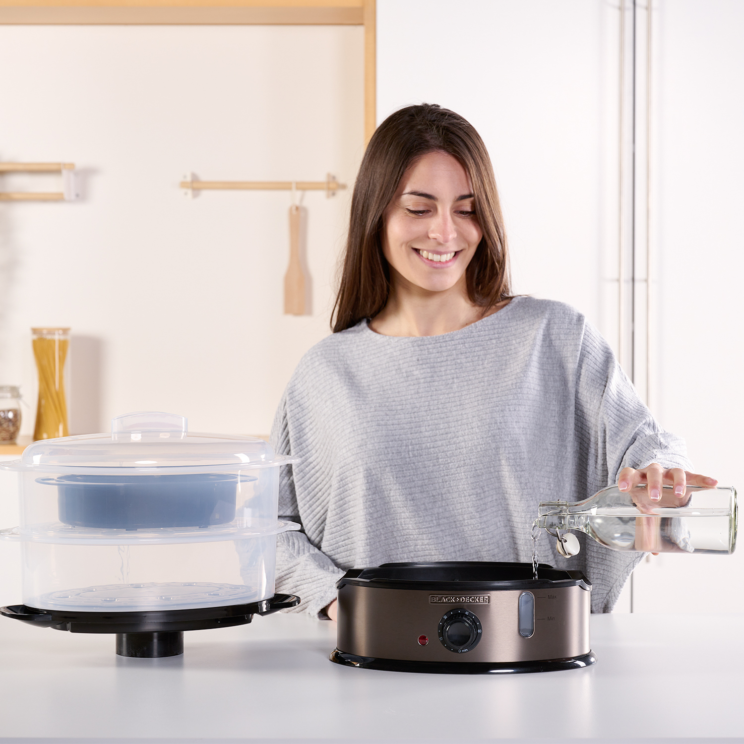 Donna versa acqua in un cuocivapore su un bancone bianco in cucina.