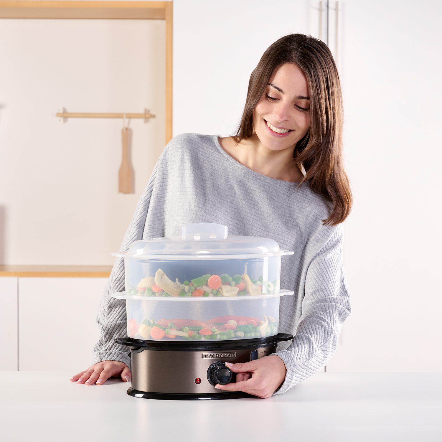 Donna che gira un quadrante su un vaporiera con verdure, su un bancone bianco.