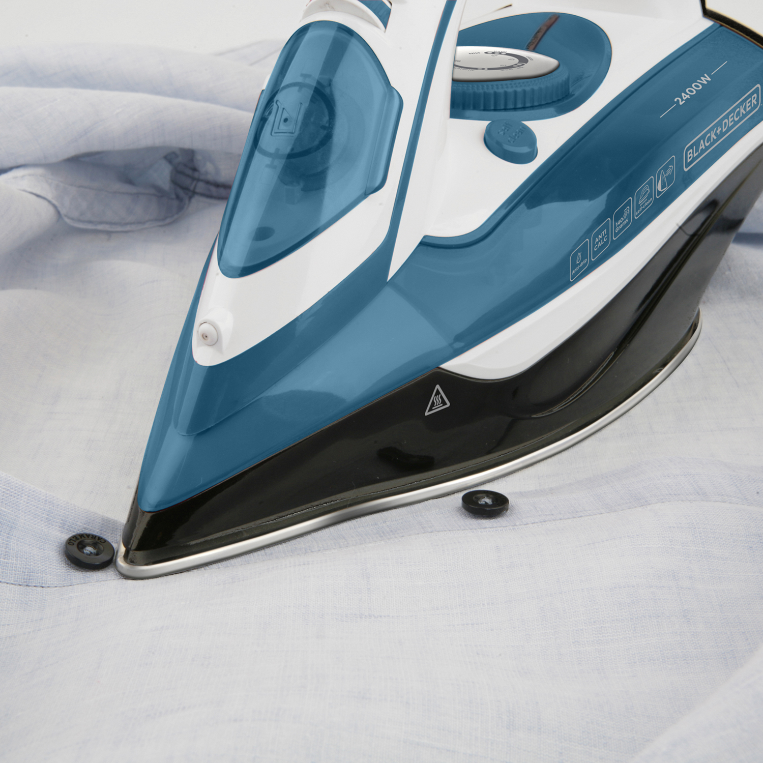 Żelazko z niebieskimi i czarnymi detalami na niebieskiej koszuli, obok guziki.