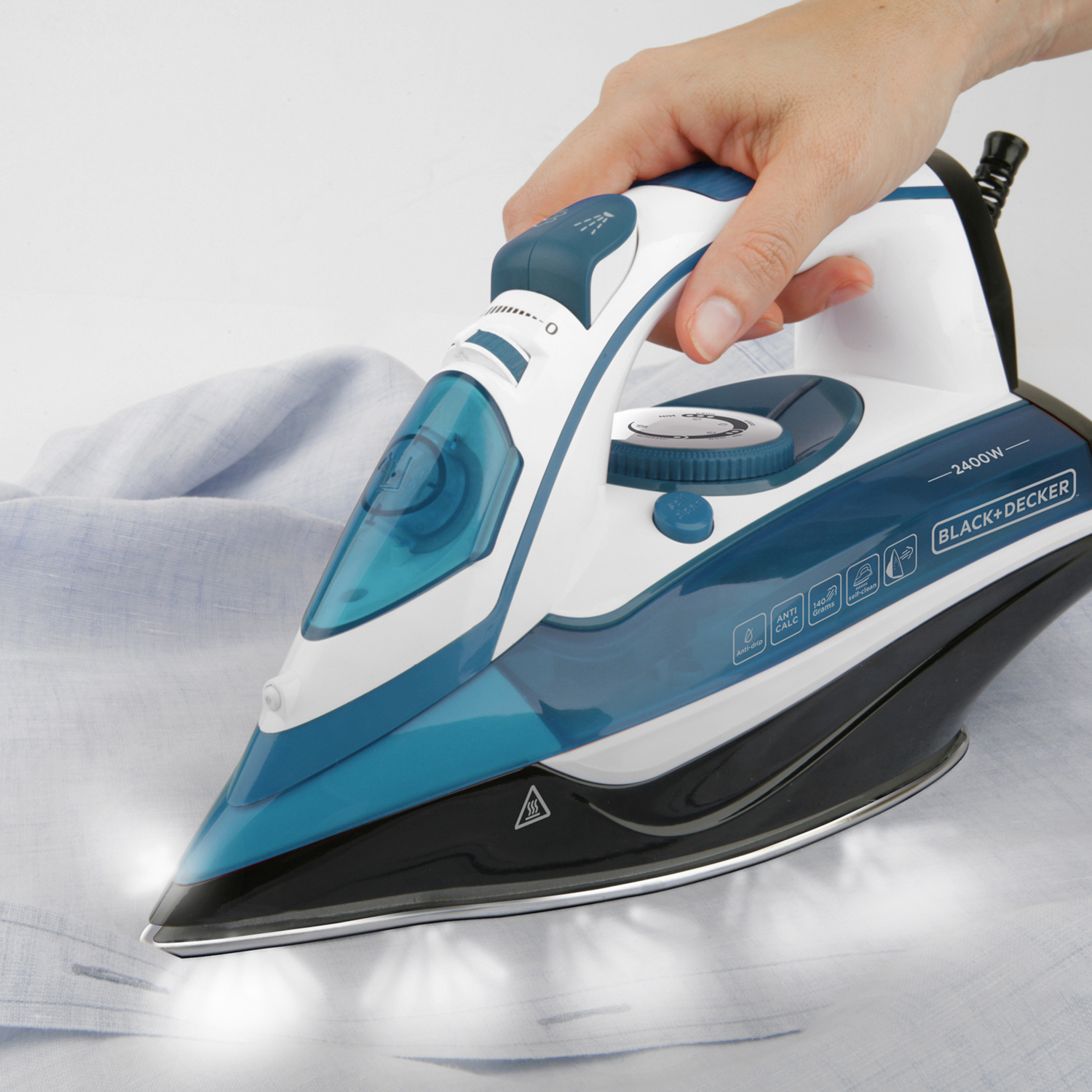 Dłoń prasuje niebieską koszulę białym i niebieskim żelazkiem. Para jest widoczna.