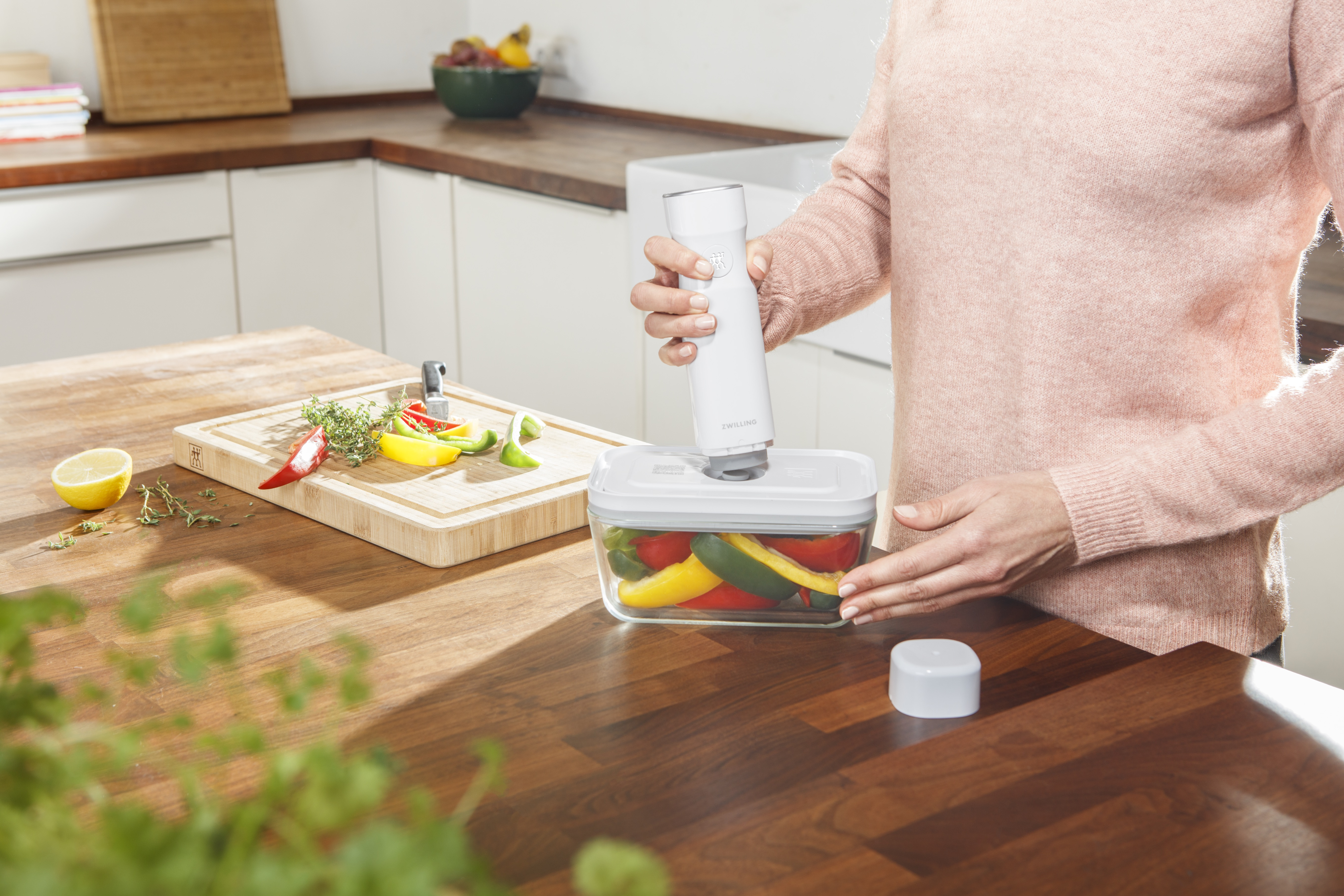 Kobieta używa zgrzewarki próżniowej na plastikowym pojemniku wypełnionym warzywami na stole.