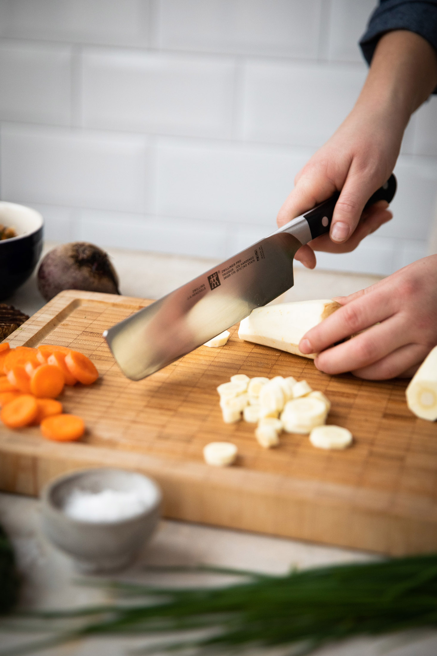 Szef kuchni kroi pasternak na drewnianej desce do krojenia z warzywami w pobliżu.