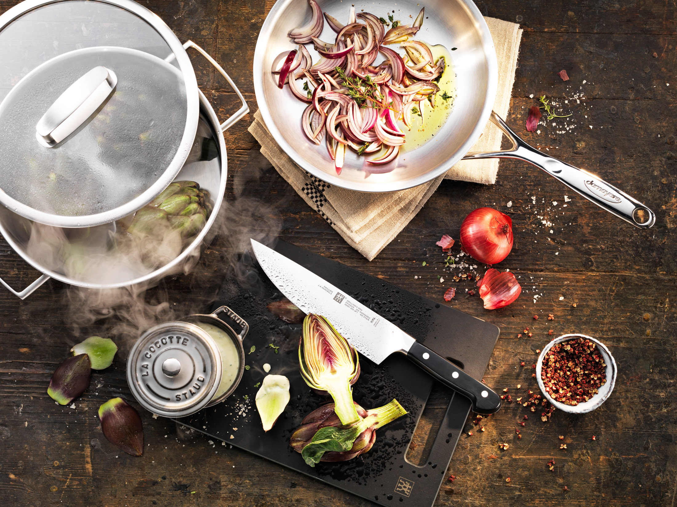 Vista dall'alto degli ingredienti di cucina. Carciofi, cipolle, un coltello e spezie su legno.